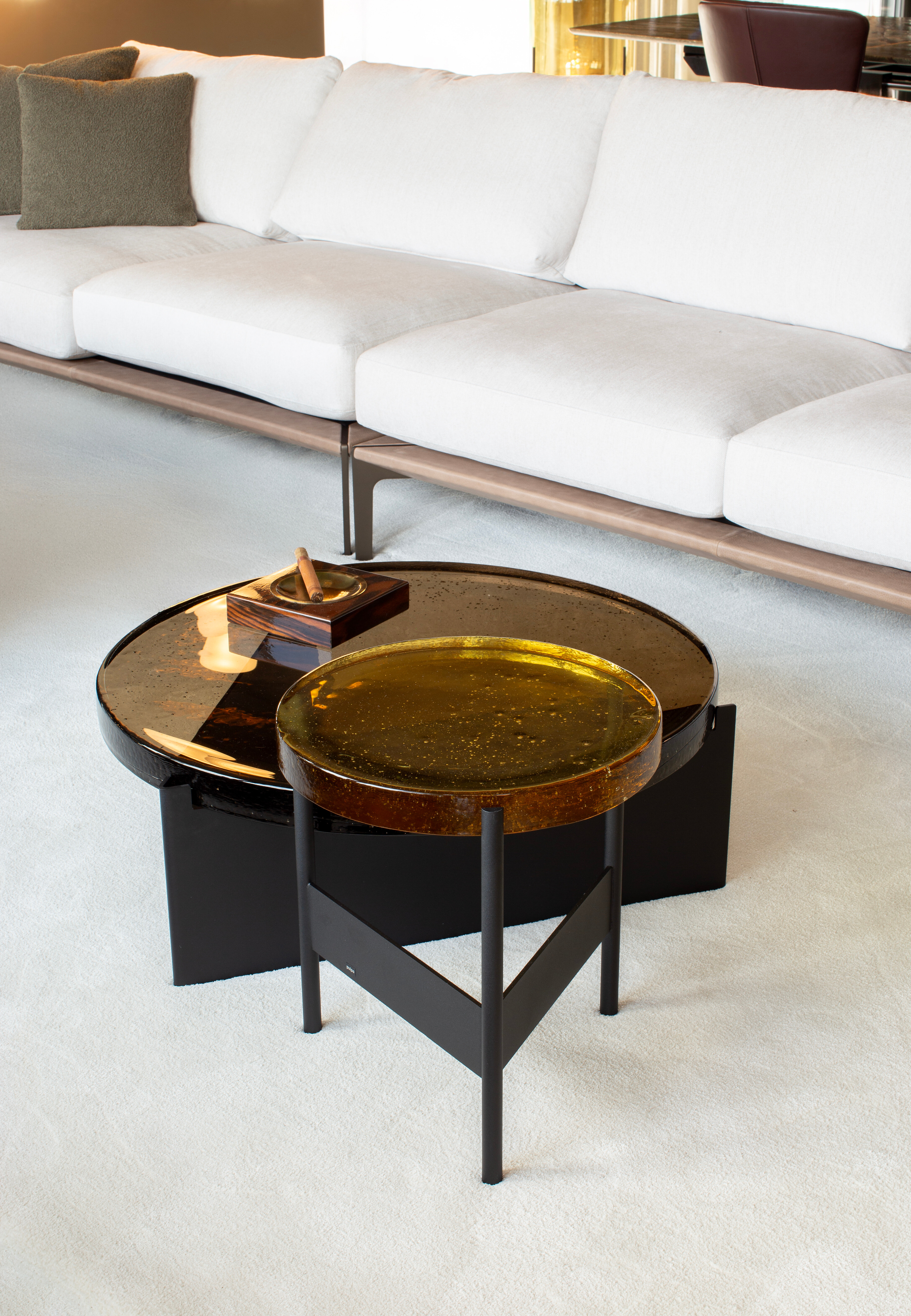 Zwei runde Beistelltische mit farbiger Glasplatte auf hellem Teppich vor Sofa