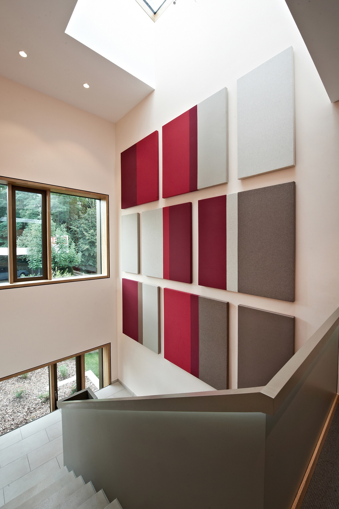 Schallschluckende Wandpaneele in Rot, Grau und Beige in einem lichtdurchfluteten Flur.