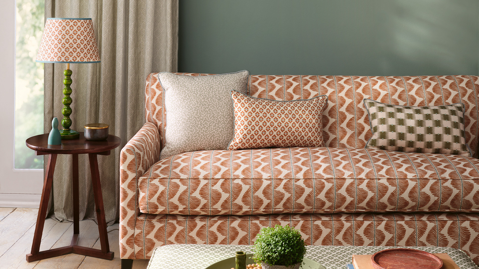 Sofa mit kleingemustertem Stoffbezug in Terrakottatönen vor grüner Wandfarbe