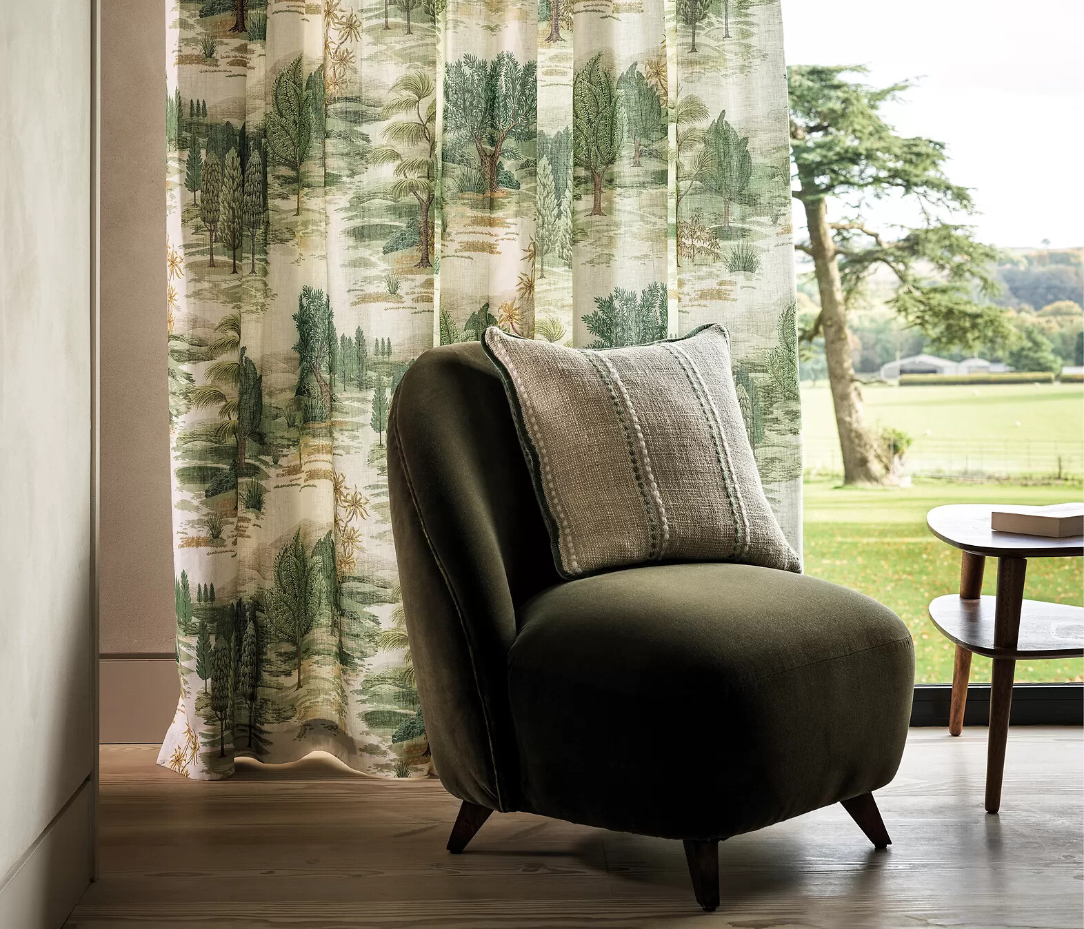 Vorhang mit grünem Landschaftsmotiv neben Sessel mit Kissen in neutralem Interieur