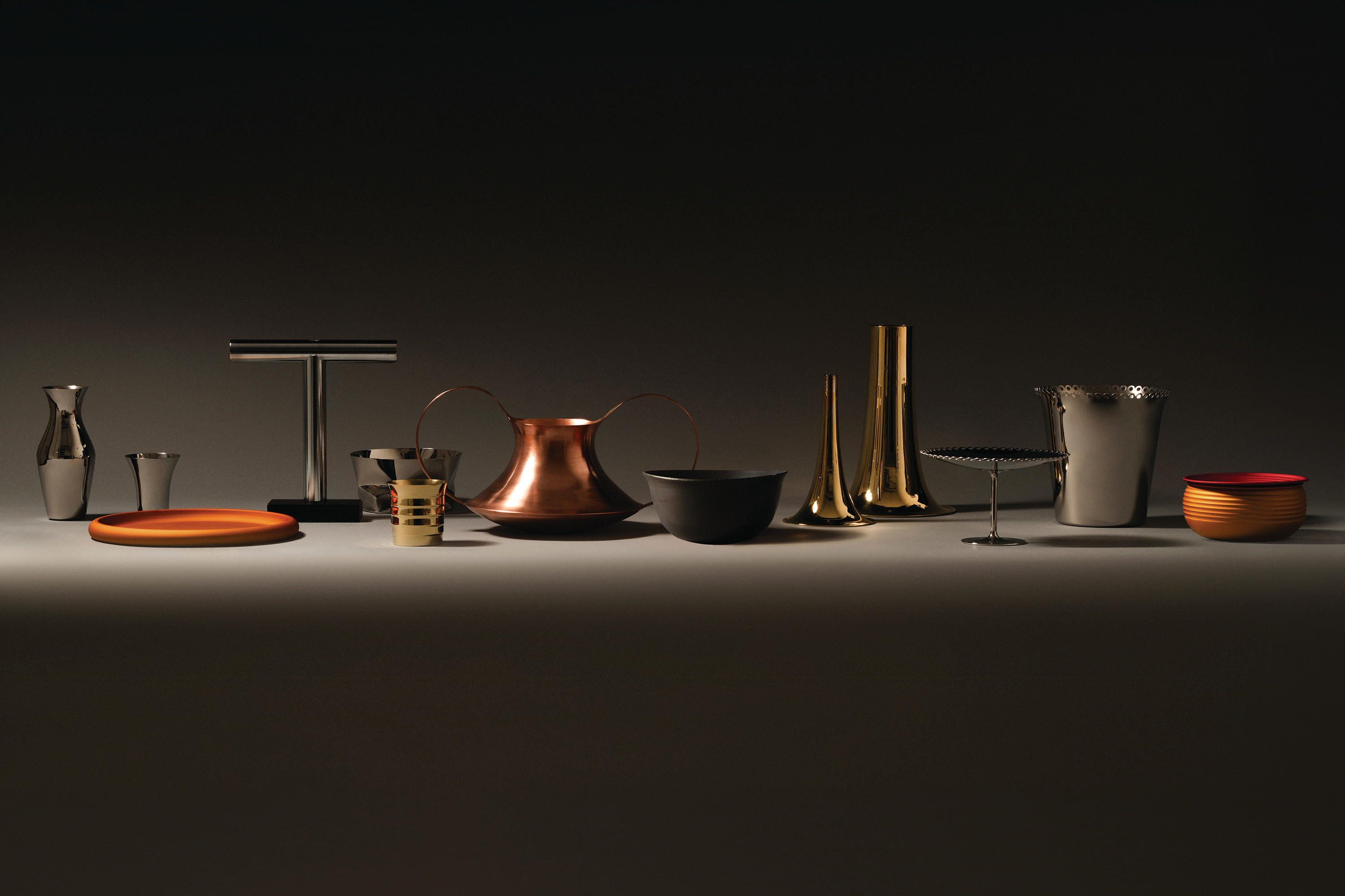 Arrangierte Accessoires und Geschirrteile aus Metall und Holz von Alessi auf dunkler Oberfläche mit Lichtakzent