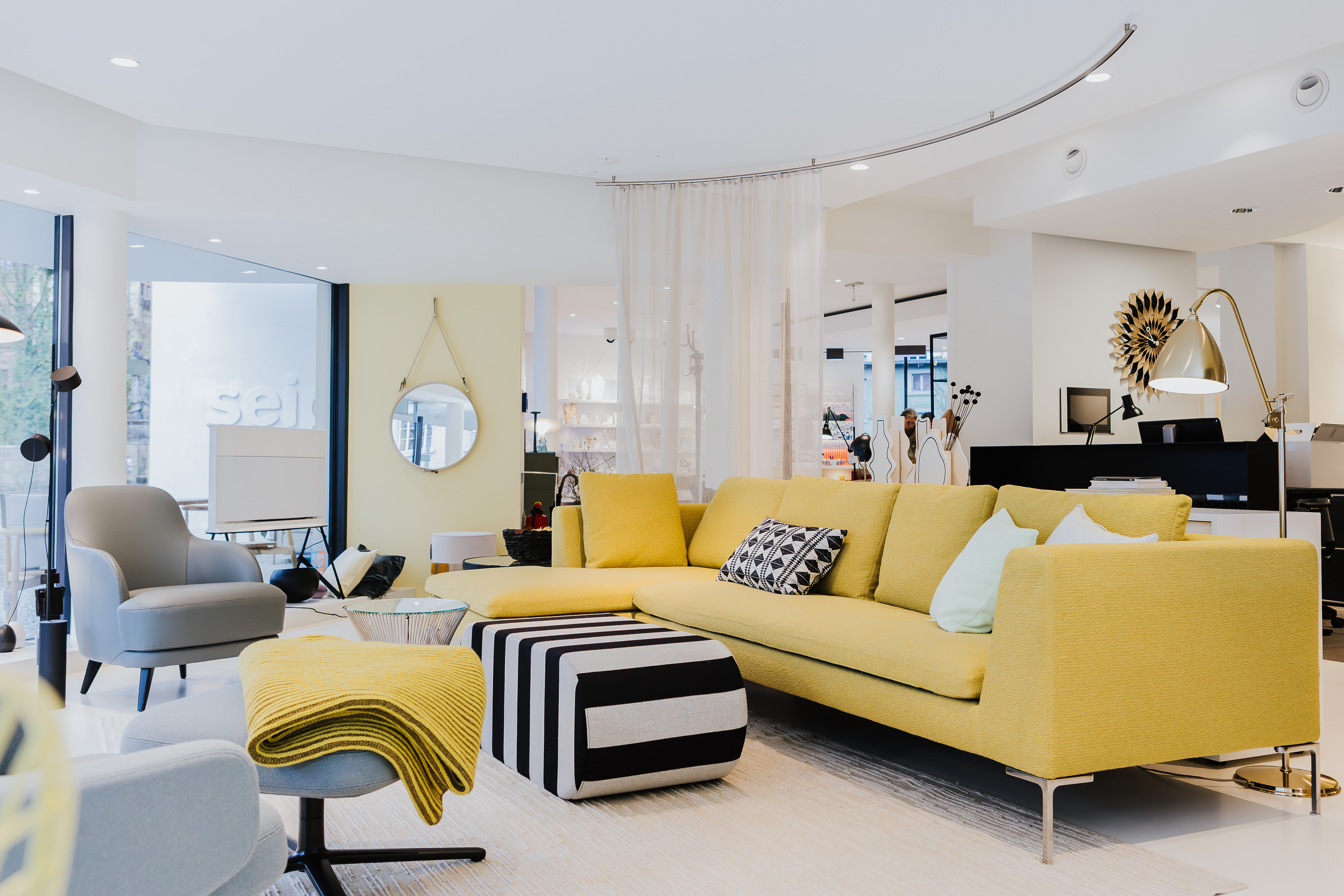 Ausstellungsszene bei Seipp Wohnen mit gelbem Sofa, grauem Sessel und grafisch gemustertem Pouf im Showroom Waldshut.
