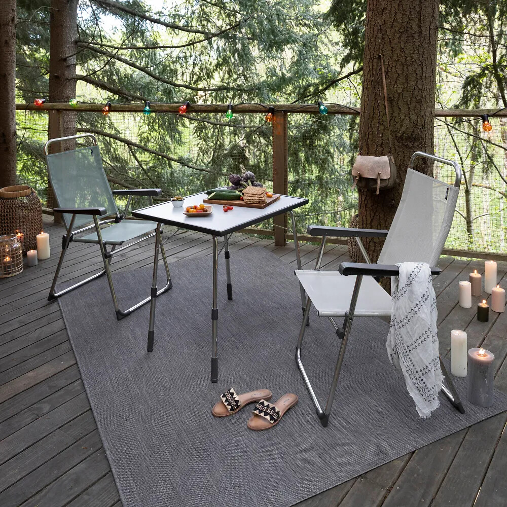 Zwei Outdoor-Klappstühle und kleiner Esstisch auf Holzplattform im Wald mit Kerzenlicht