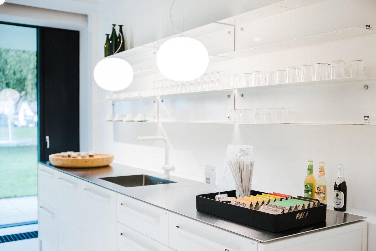 Küchenbereich im Café Supernormal mit weißer Einrichtung und modernen Leuchten.