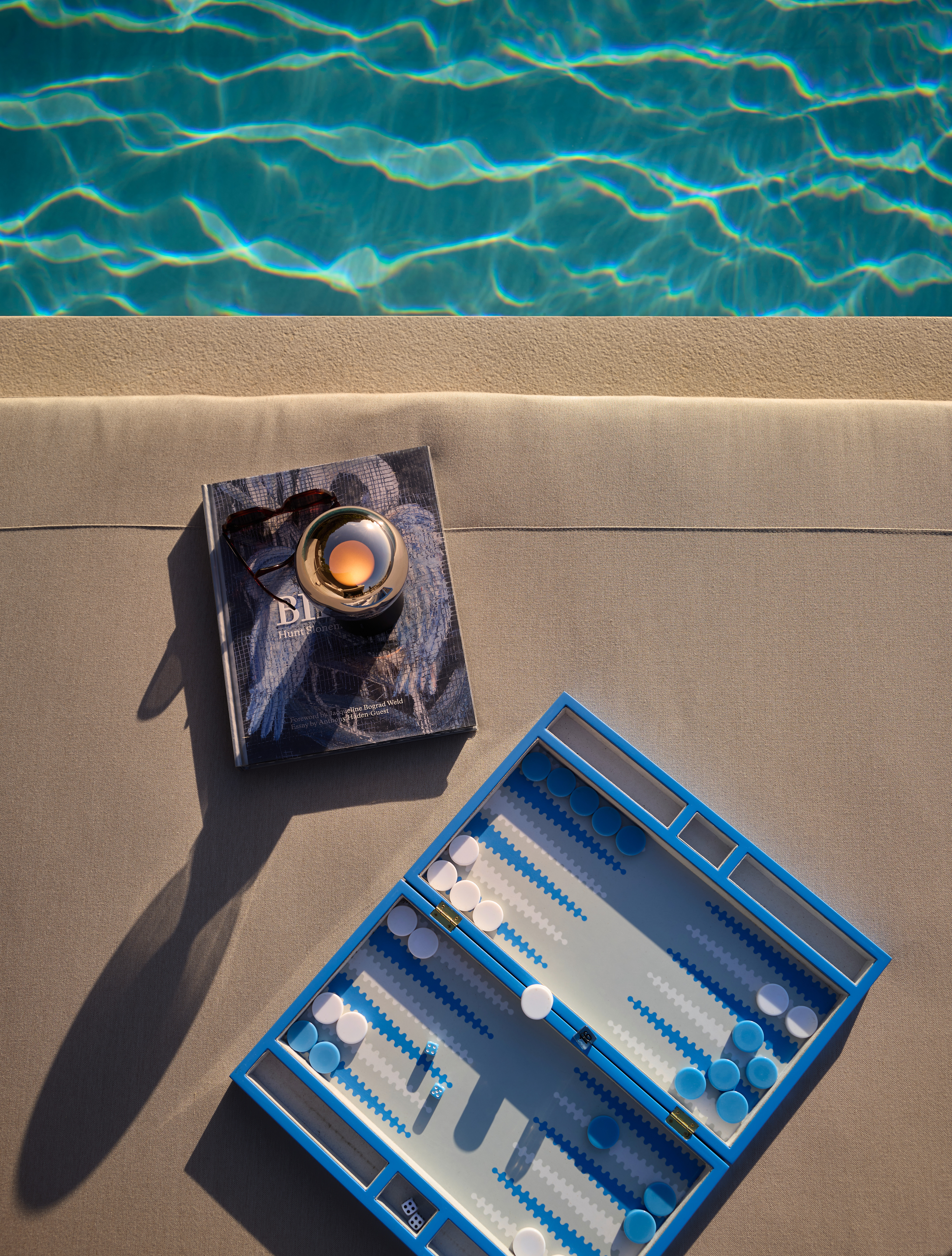 Poolliege mit Backgammon-Spiel, Buch und Occhio Leuchte Luna pura in abendlicher Stimmung