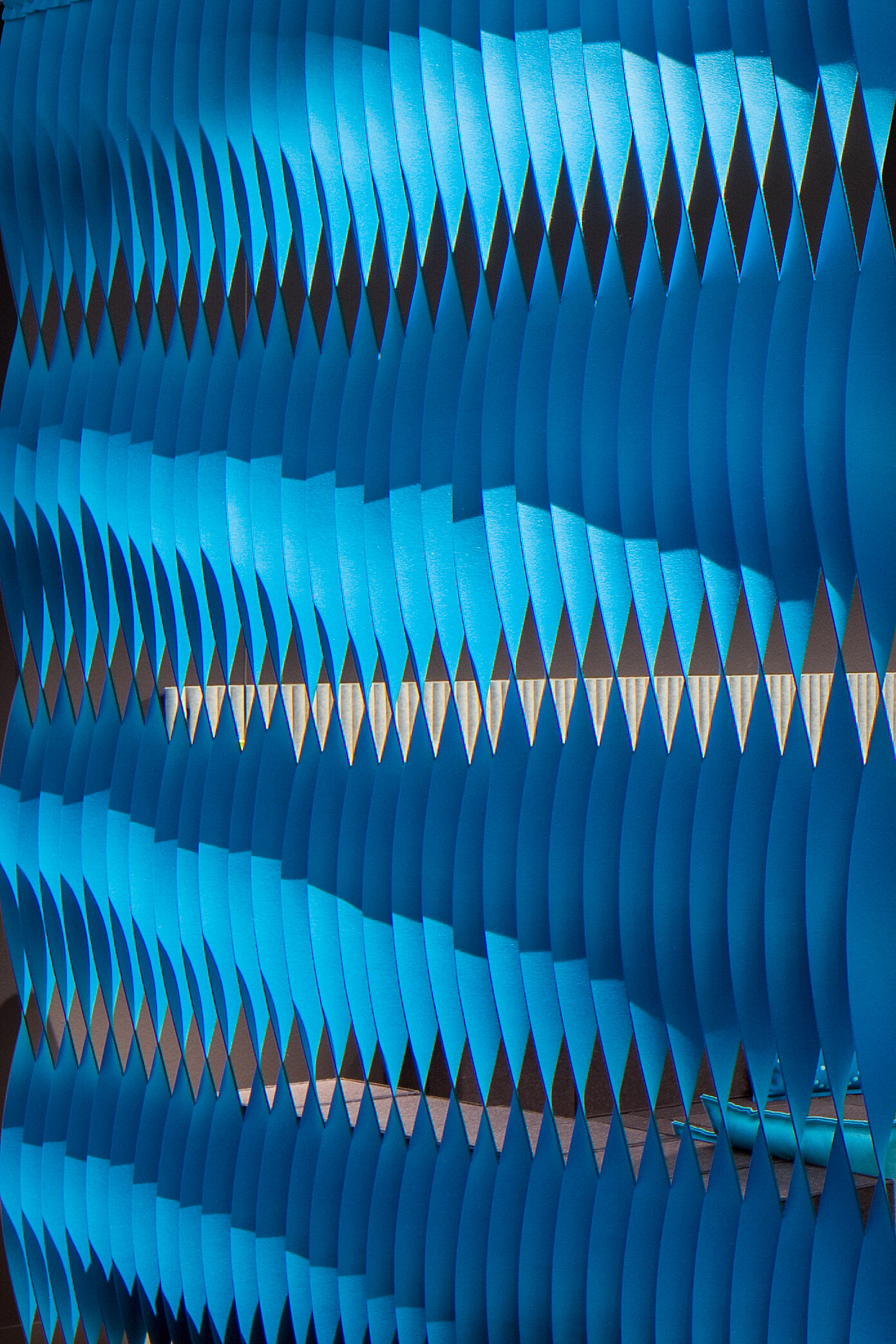 Blau gefärbte Akustikelemente in wellenartiger Anordnung vor dunklem Hintergrund