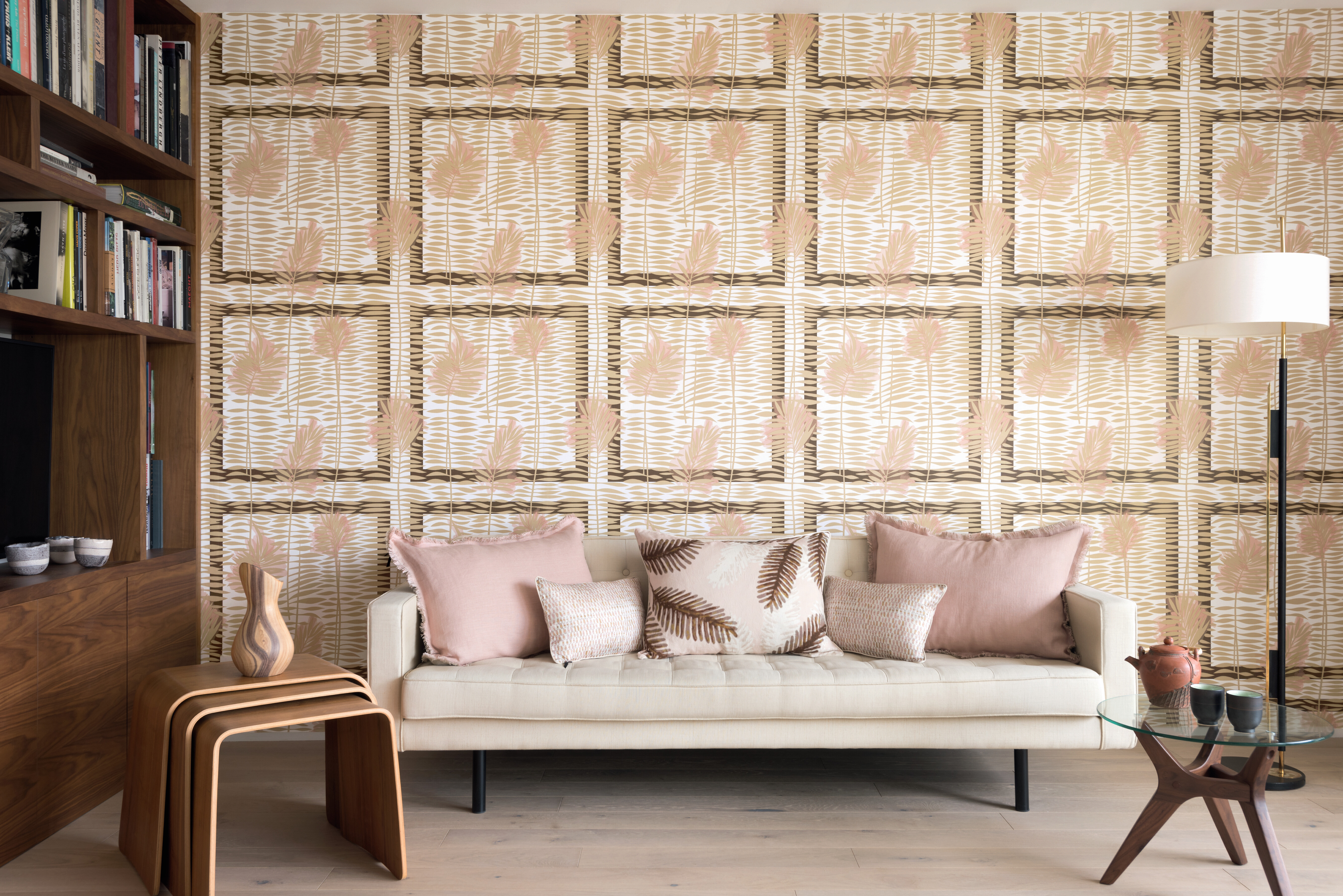 Beiger Bezugstoff auf Sofa vor grafischer Tapete in Creme- und Rosétönen mit Farnmotiv