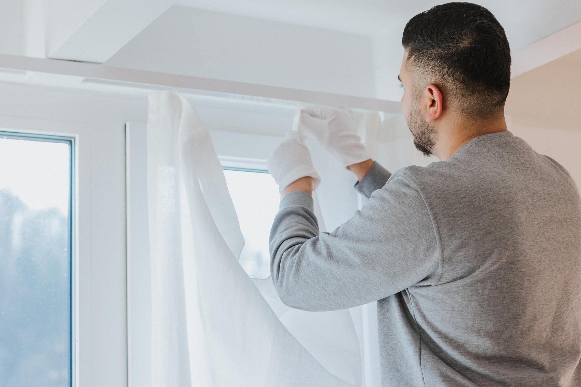 Ein Mitarbeiter von Seipp Wohnen montiert mit weißen Handschuhen einen transparenten Vorhang