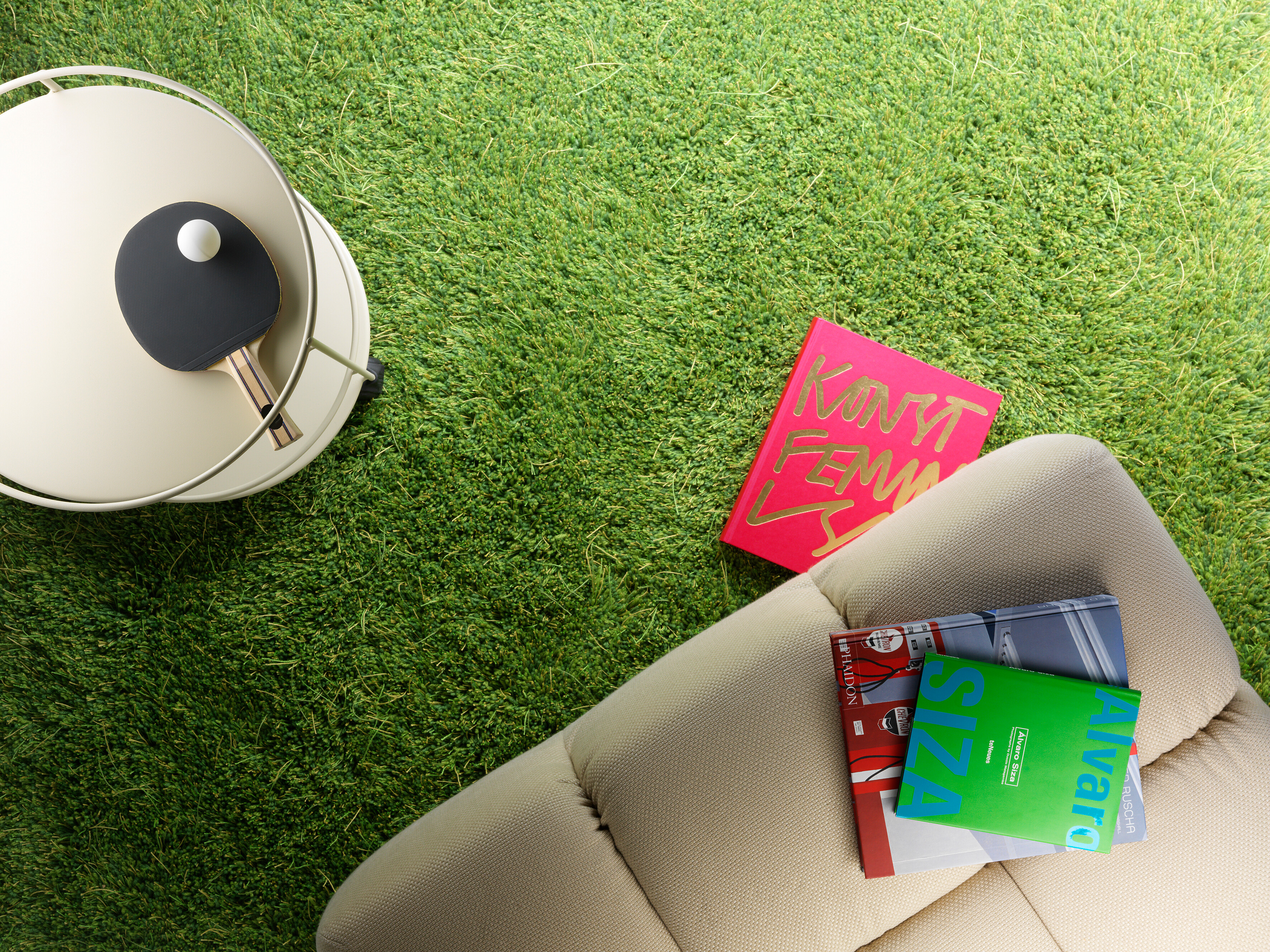 Grüner Teppich in Grasoptik mit Büchern und Tischtennisschläger auf hellem Beistelltisch