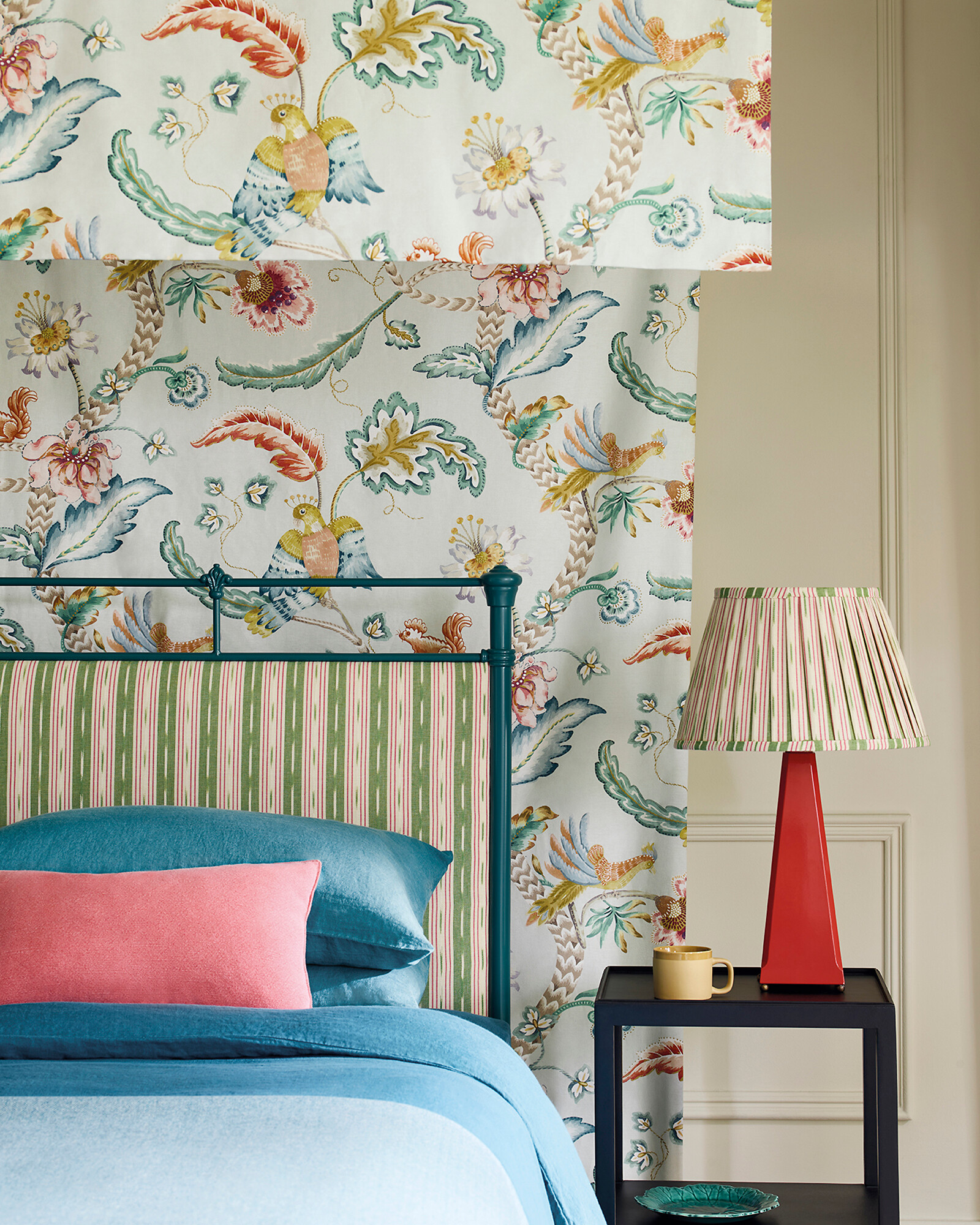 Bett mit farbenfroher Tapete, gestreifter Lampe und Bezug im floralen Mustermix