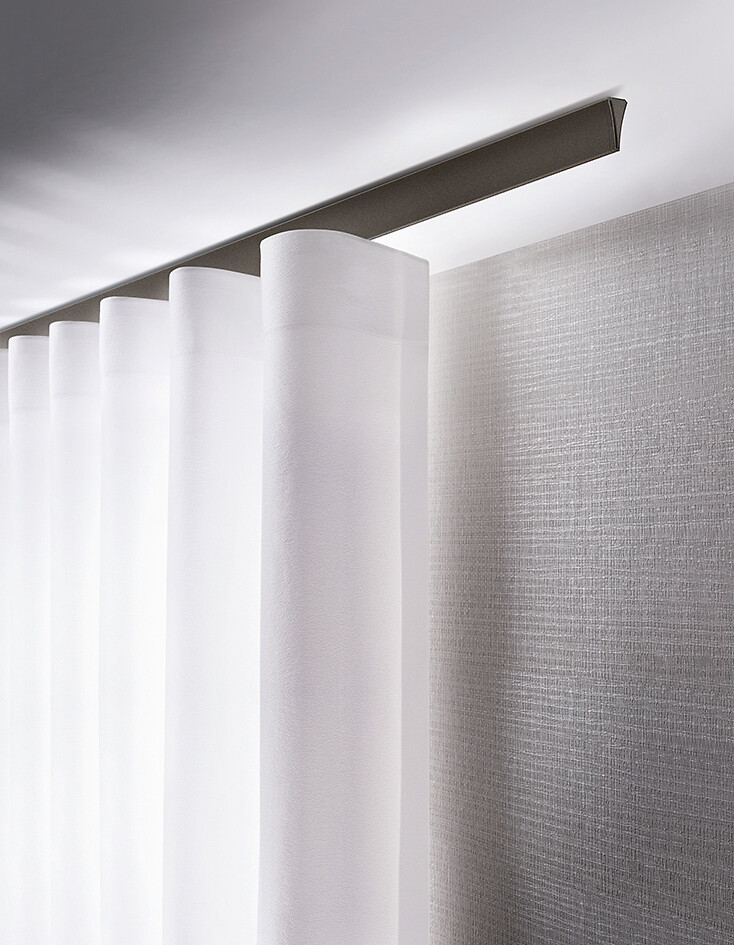 Weiße Gardine mit gleichmäßiger Wellenführung an flacher Deckenschiene