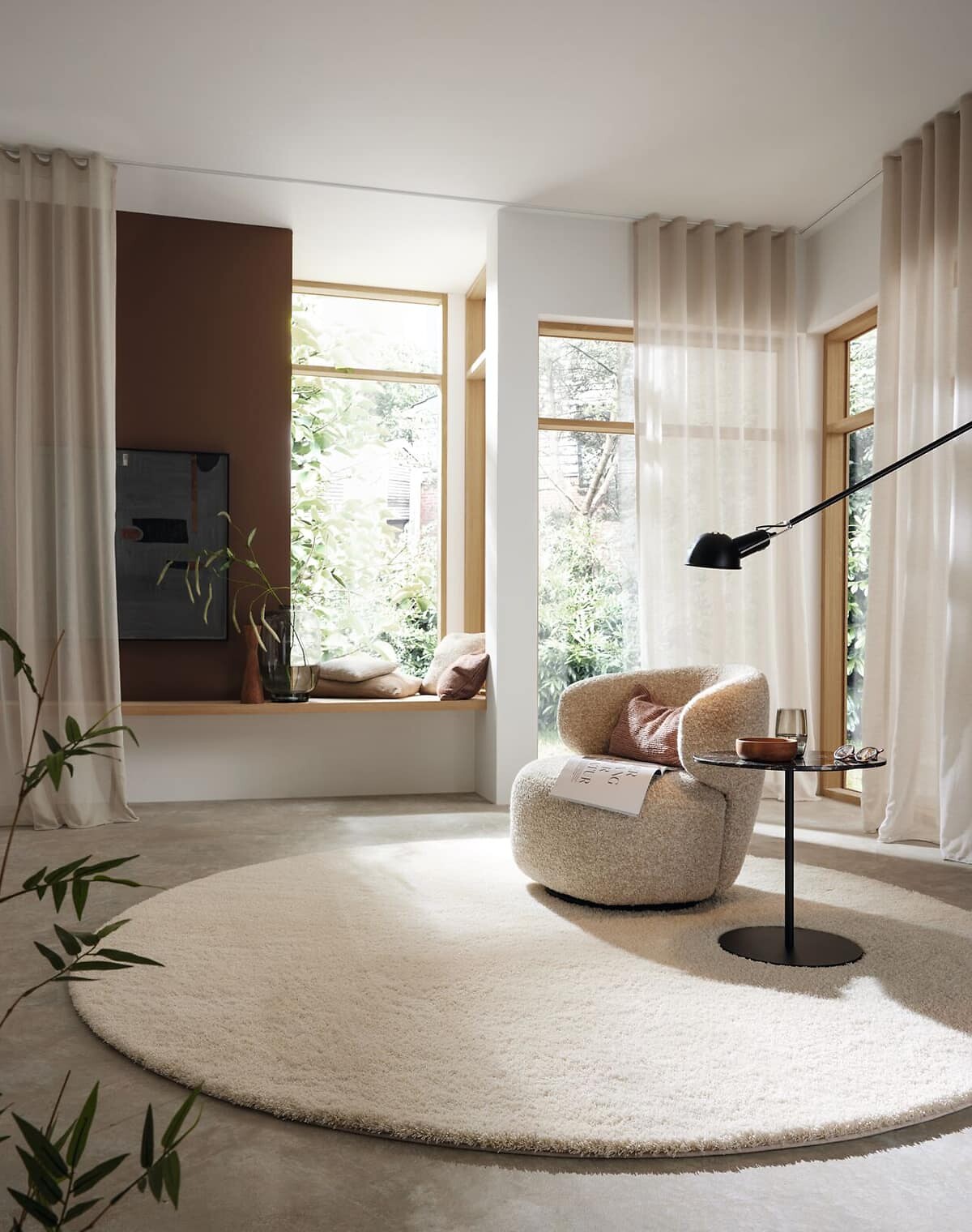 Runder, hochfloriger Teppich in Cremeweiß in hellem Raum mit bodentiefen Fenstern