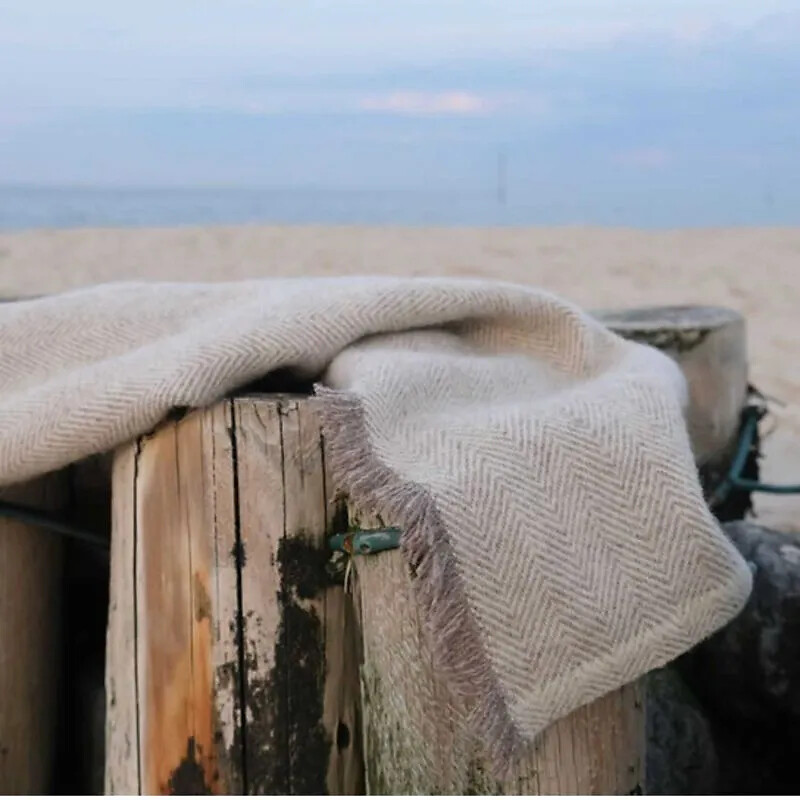 Beige Wolldecke mit Fischgrätmuster liegt locker über einem Holzpfosten
