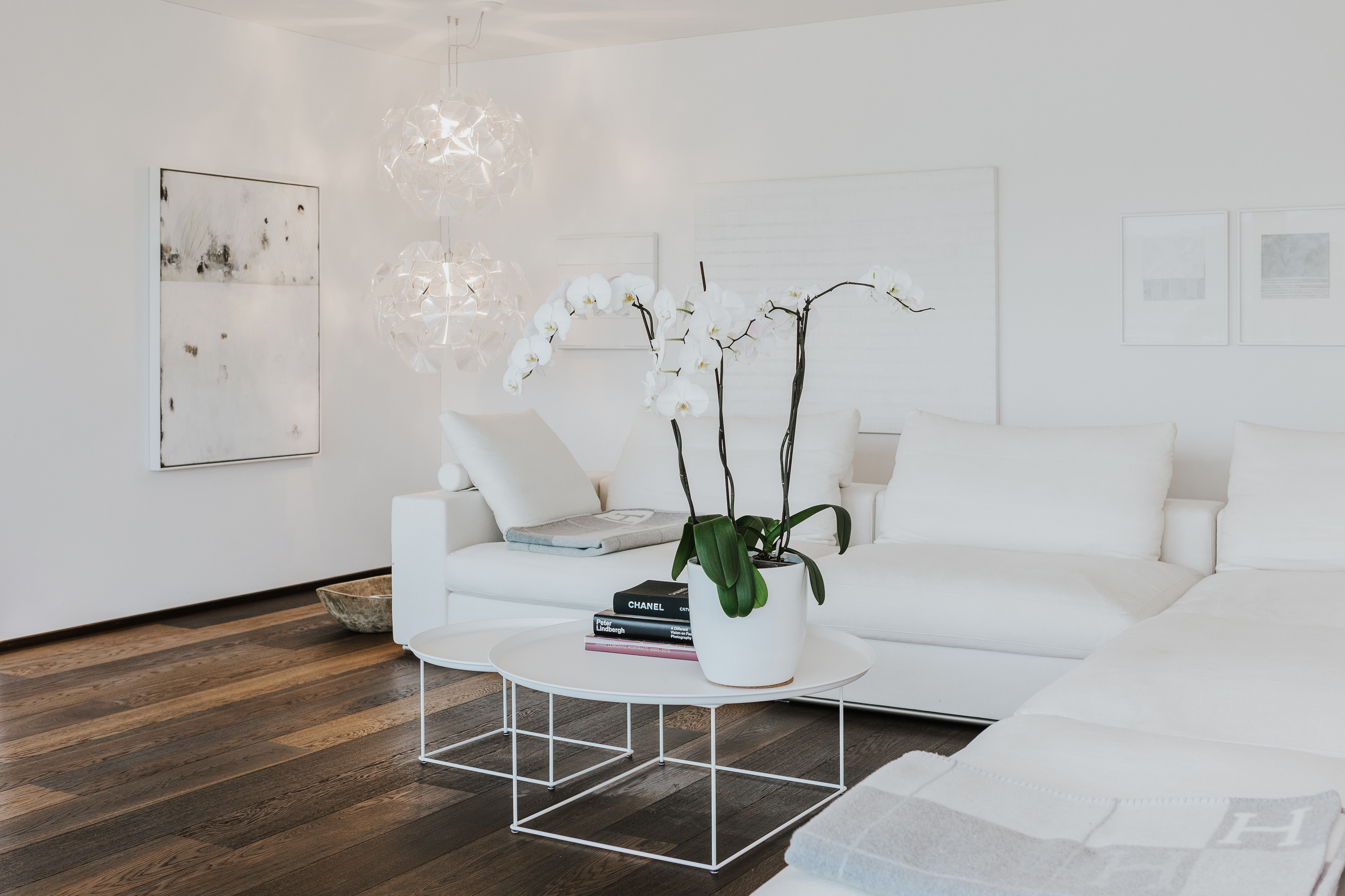 Wohnbereich in Weiß mit Sofalandschaft, dunklem Holzboden, filigranen Beistelltischen und Orchidee als Blickfang.