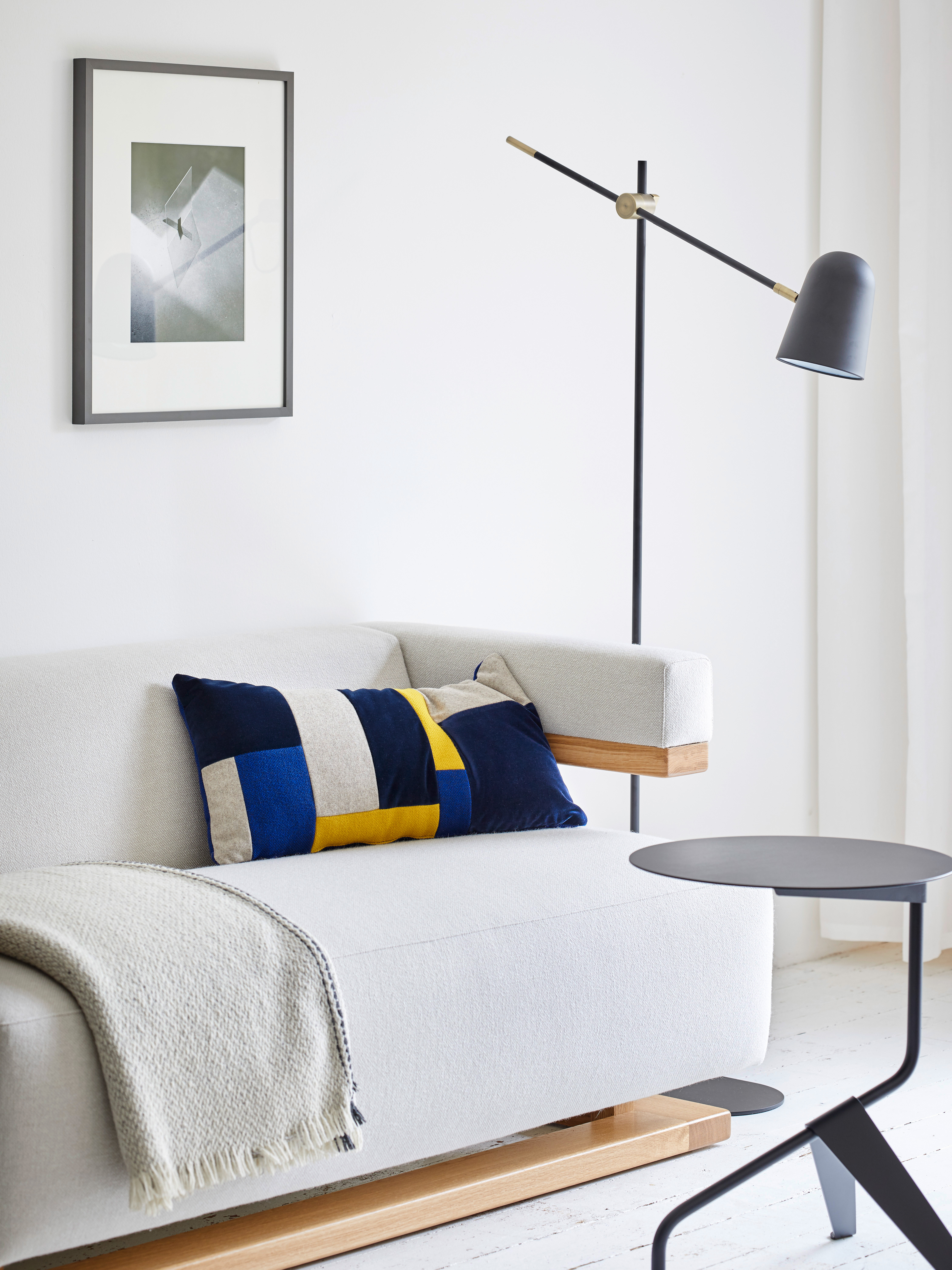 helles Sofa mit Holzelementen und schwarzer Beistellstuhl und Leuchte in Wohnzimmer