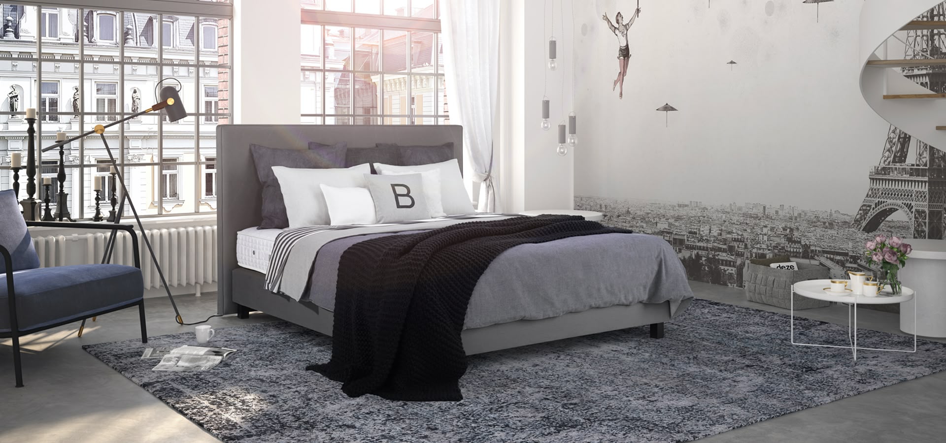 Boxspringbett mit grauem Kopfteil vor großflächiger Paris-Fototapete in hellem Raum