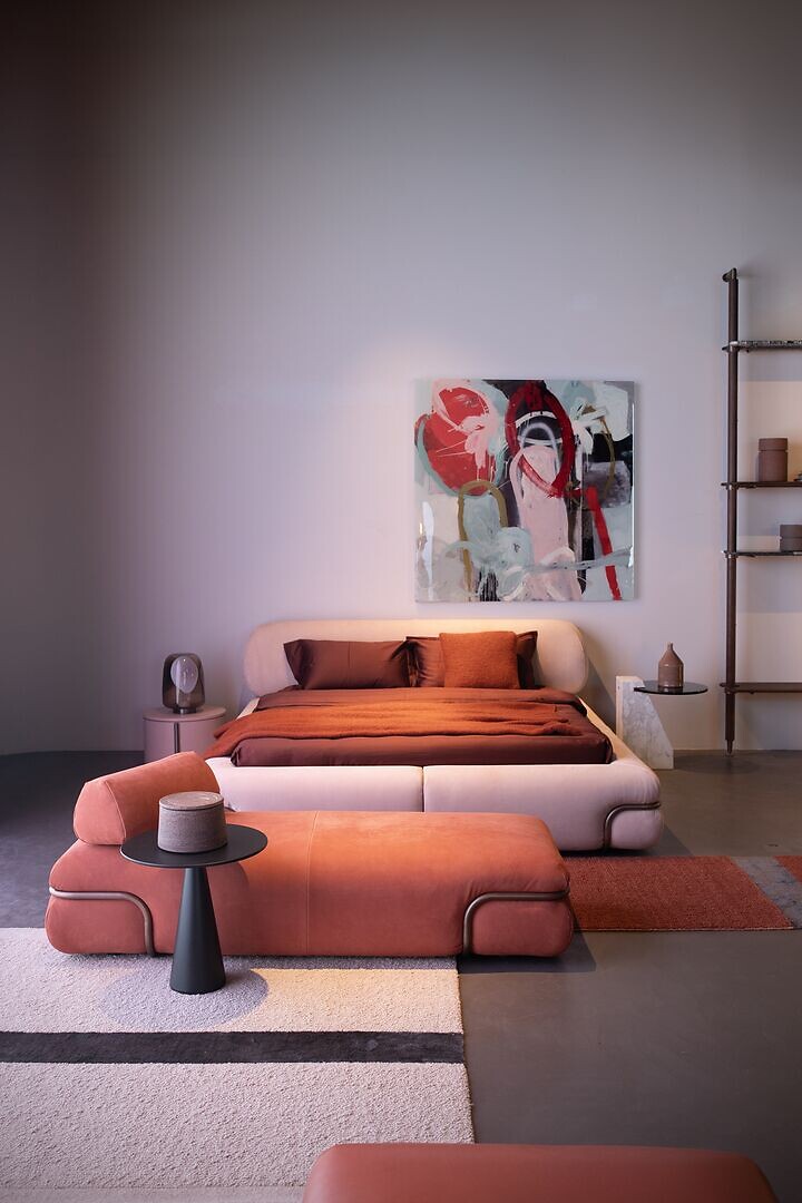 Polsterbett in Rosétönen mit passendem Hocker in modernem Schlafzimmerambiente