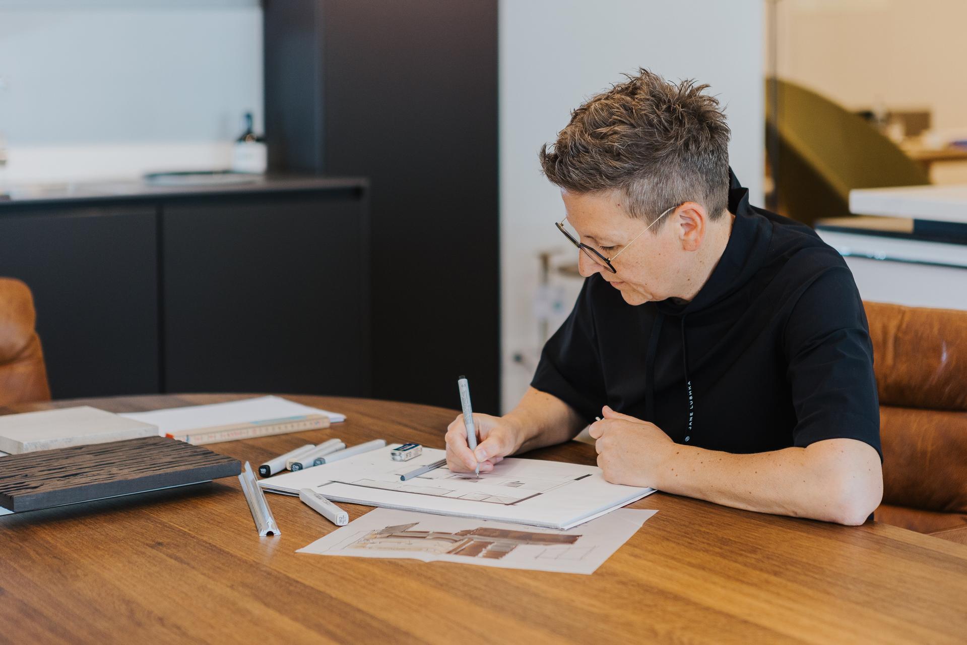 Person bei der Küchenplanung am Tisch mit Zeichnungen, Mustern und Stift in konzentrierter Haltung