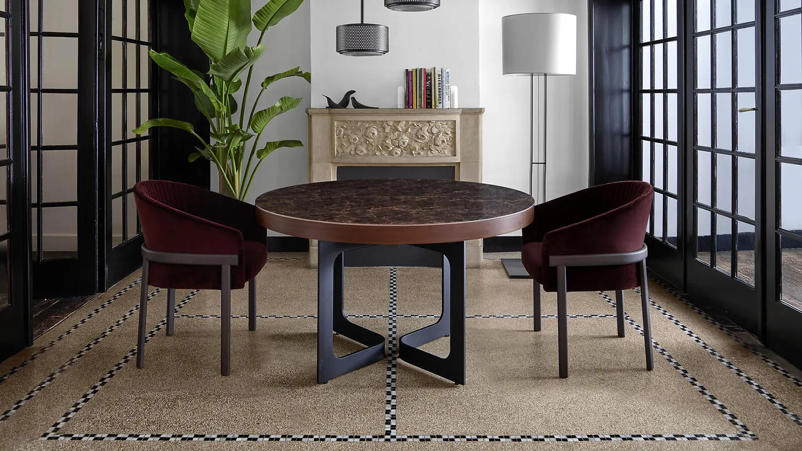 Runder Tisch mit dunkler Platte und zwei samtigen Sesseln in burgunderrot in einem eleganten Raum.