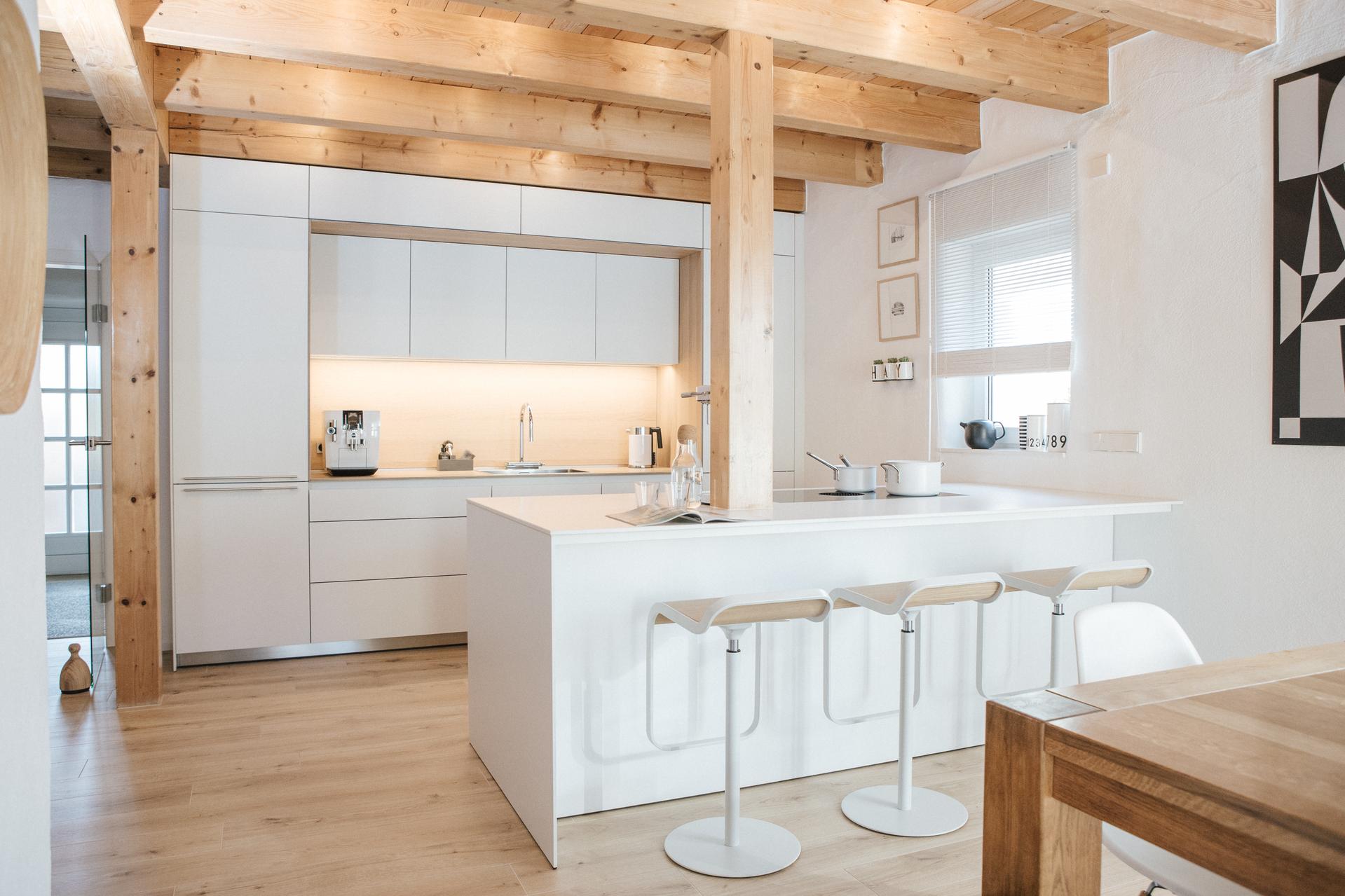 bulthaup b3 Küche mit Kochinsel in modernem Wohnraum mit Holzbalkendecke, Barhockern und Esstisch.