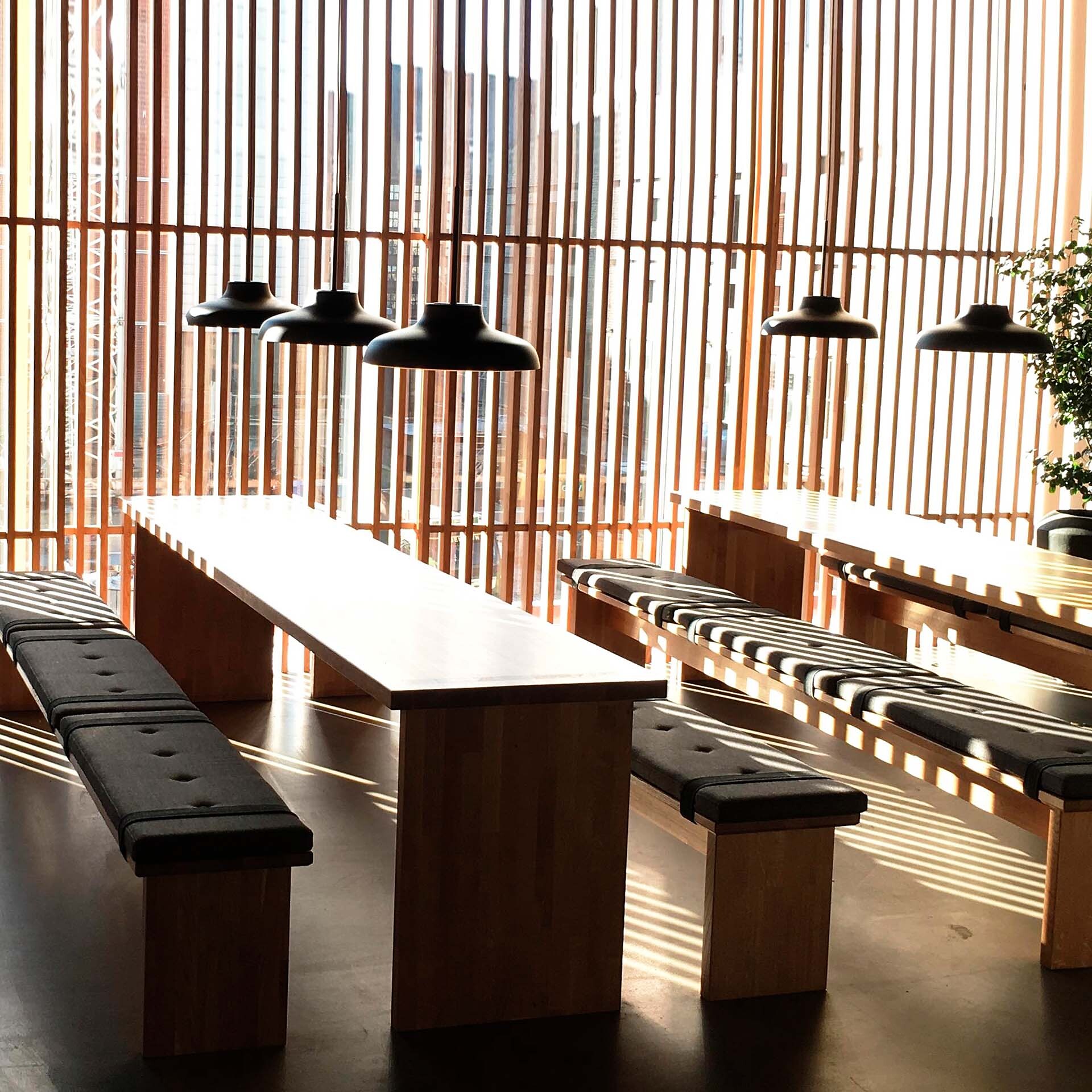 Holzverkleideter Raum mit Bänken, Tisch und schwarzen Pendelleuchten von RUBN