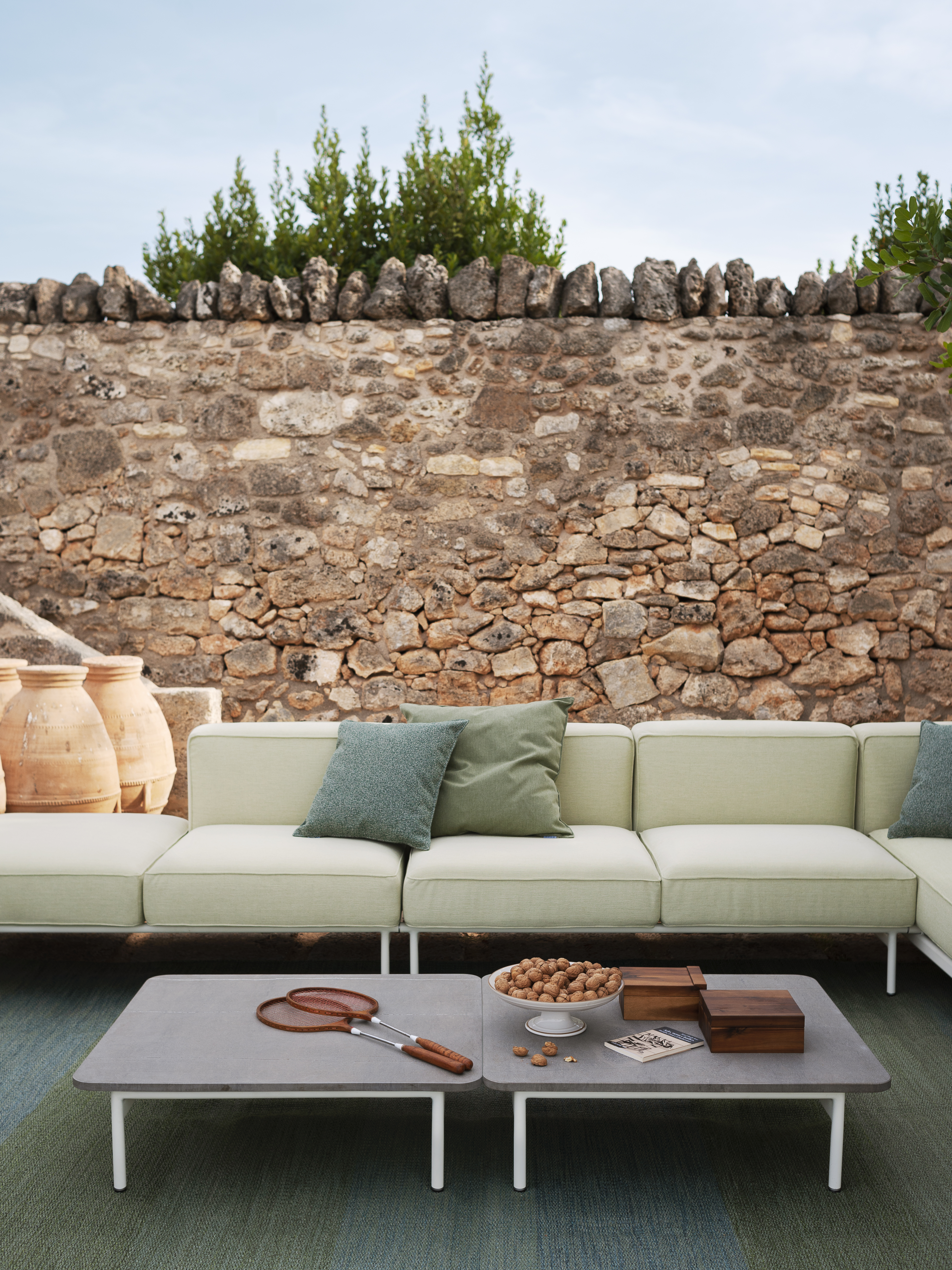 Helles Outdoor-Sofa mit grünen Kissen und Couchtisch vor Natursteinmauer