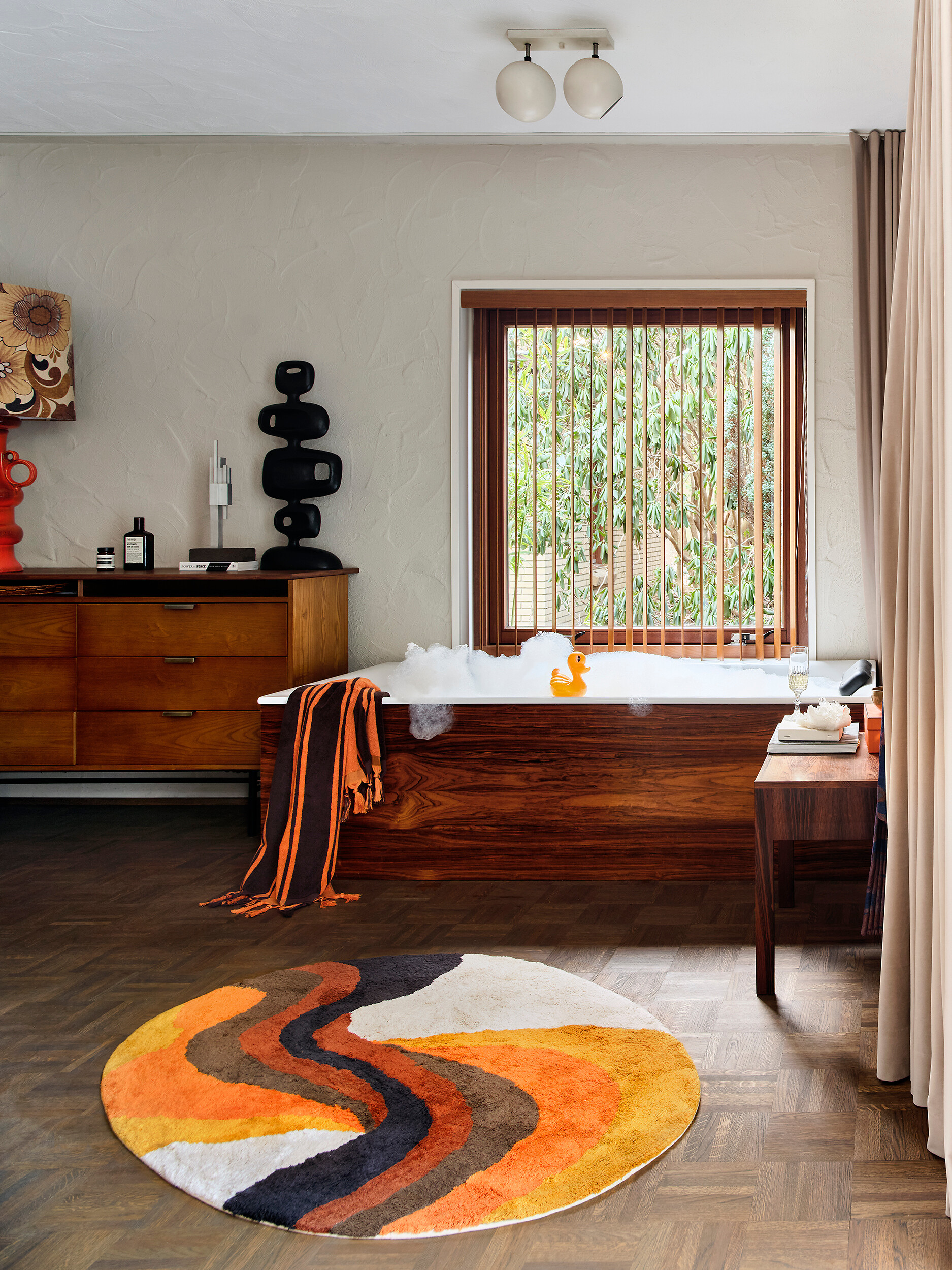 Rundes Teppichmotiv in Orange- und Brauntönen vor Badewanne mit Holzverkleidung
