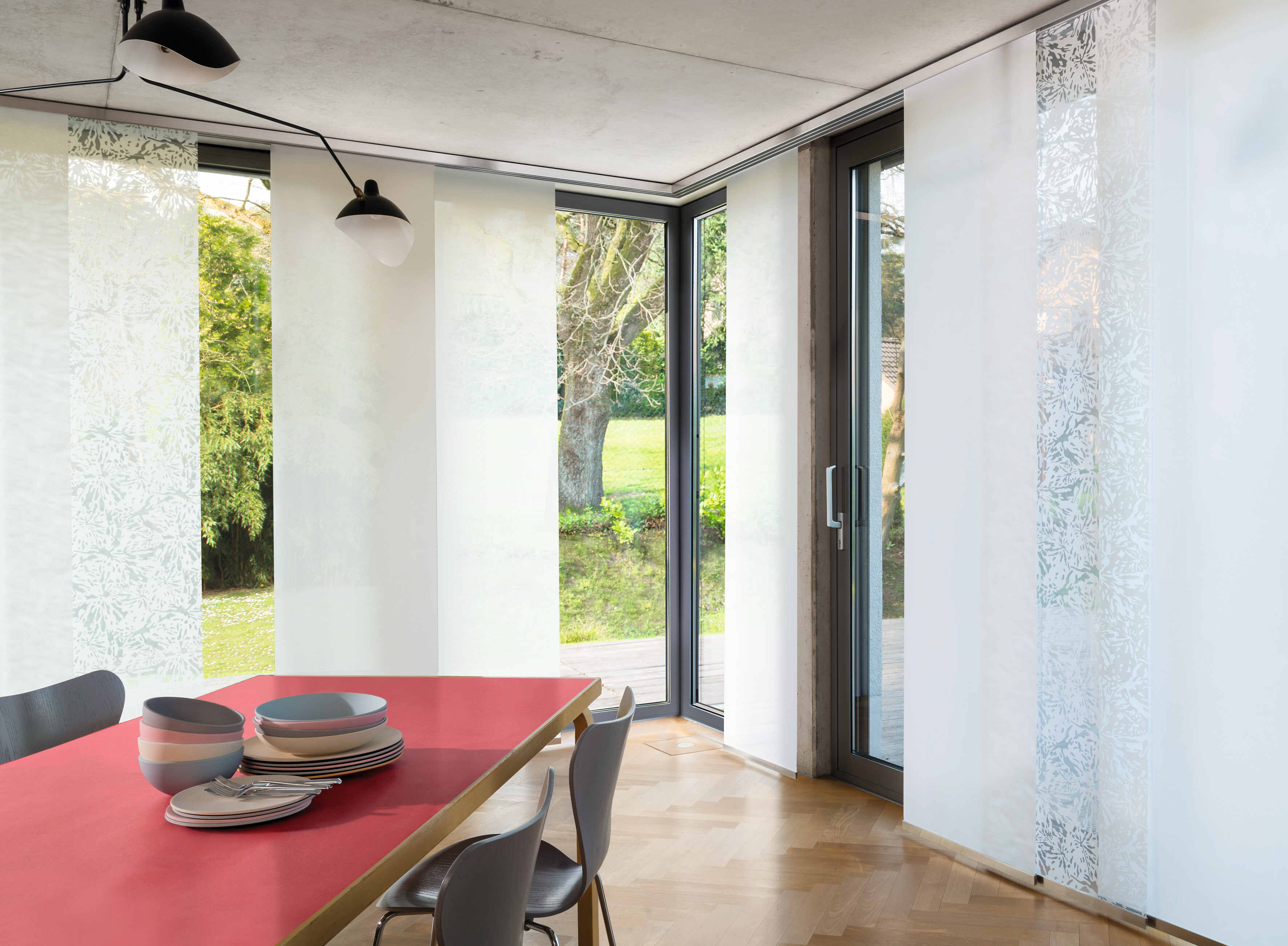 Dezente Stoffpaneele mit floralem Muster vor großflächiger Verglasung