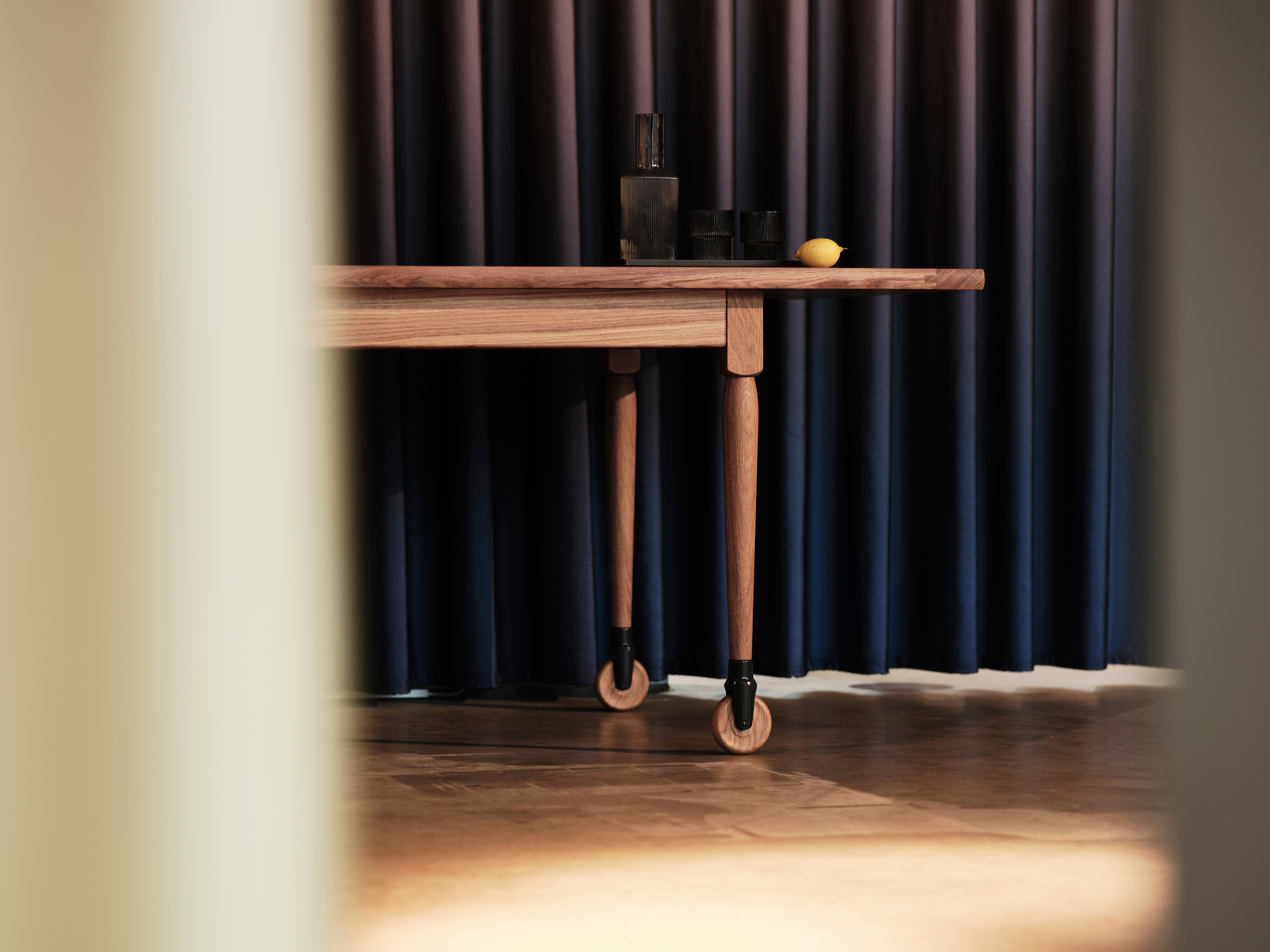 Shaker-Tisch aus Holz mit charakteristischen Rollenbeinen, im Vordergrund unscharfer Durchblick.