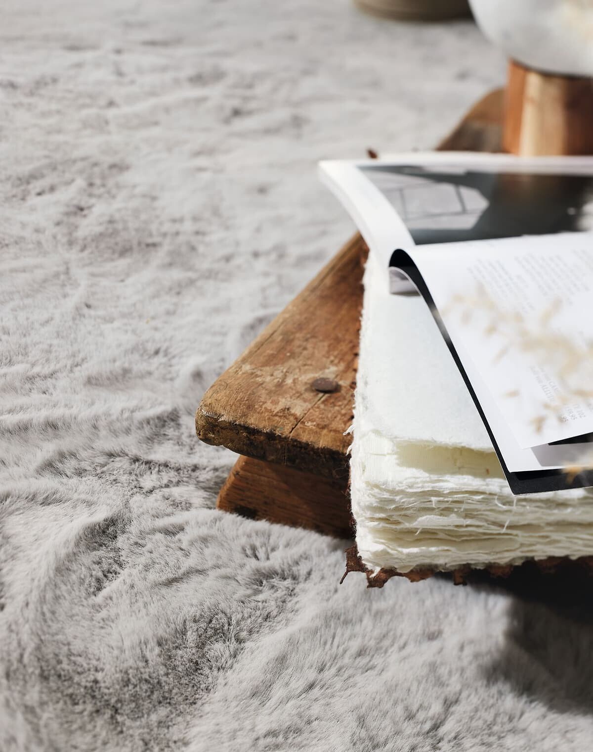 Detail eines flauschigen Teppichs in Silbergrau mit Holzbank und Magazin darauf