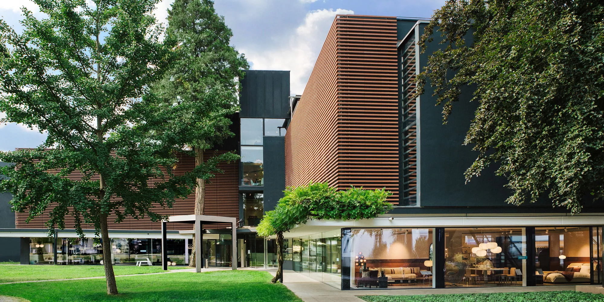 Seipp Wohnen in Tiengen mit moderner Holzlamellen-Fassade und großer Fensterfront, umgeben von Grünfläche und Bäumen bei Tageslicht.