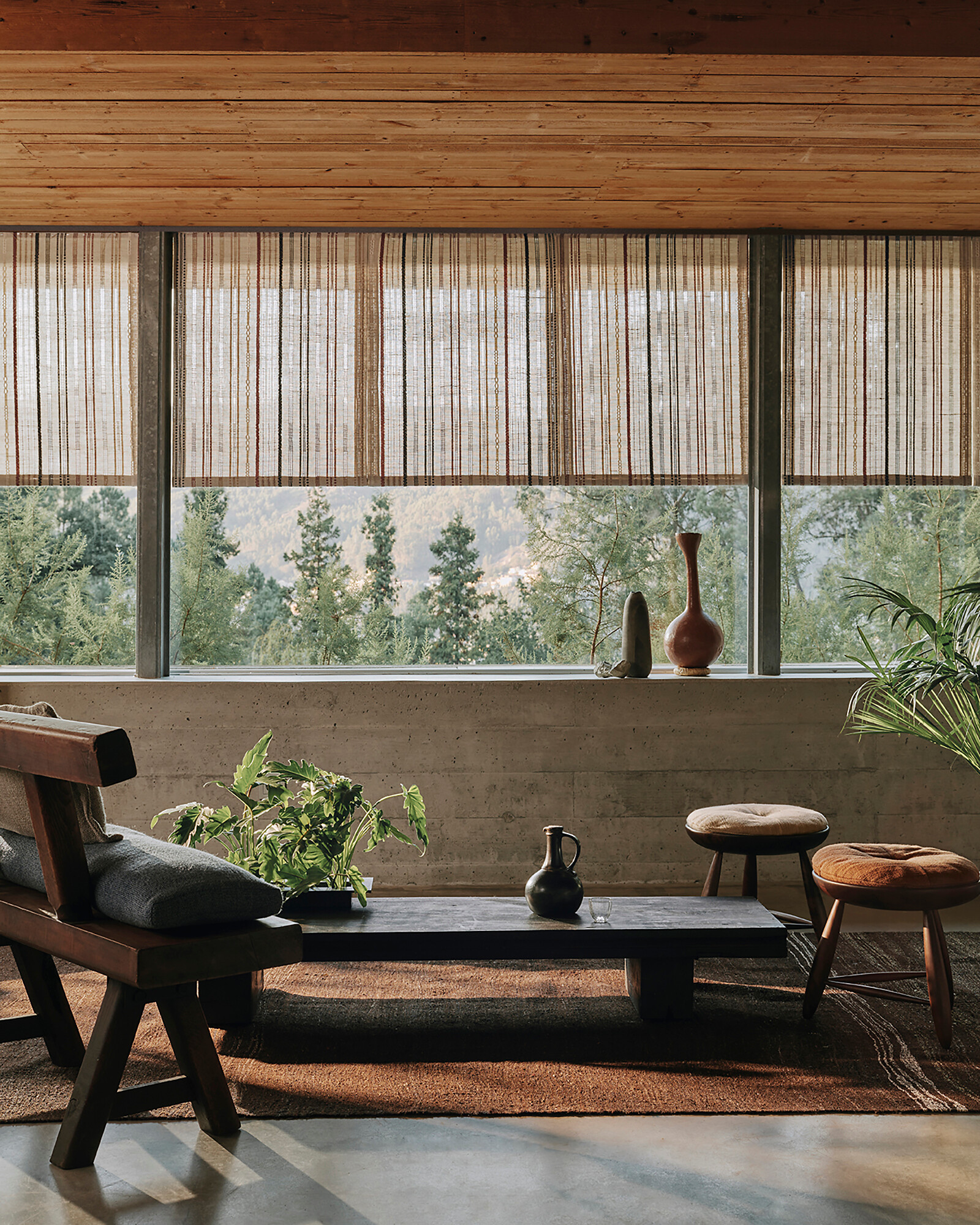 Wohnraum mit niedrigen Sitzmöbeln, schmalem Tisch und textilen Raffrollos