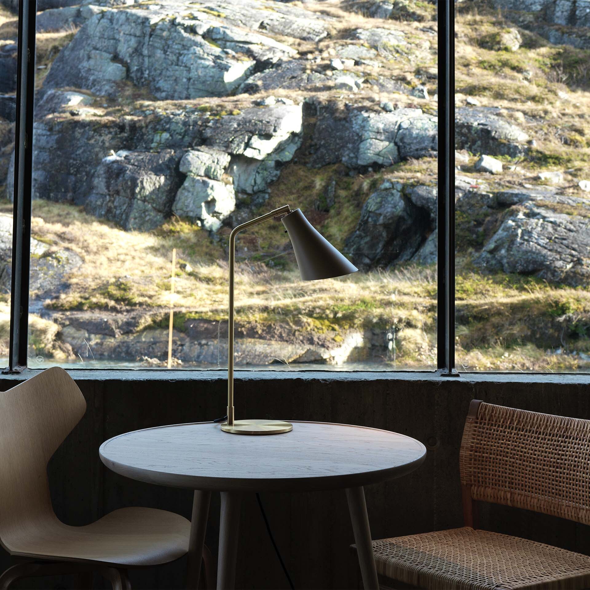 Miller Table Tischleuchte mit geneigtem Schirm auf rundem Tisch vor Fenster mit Felsblick