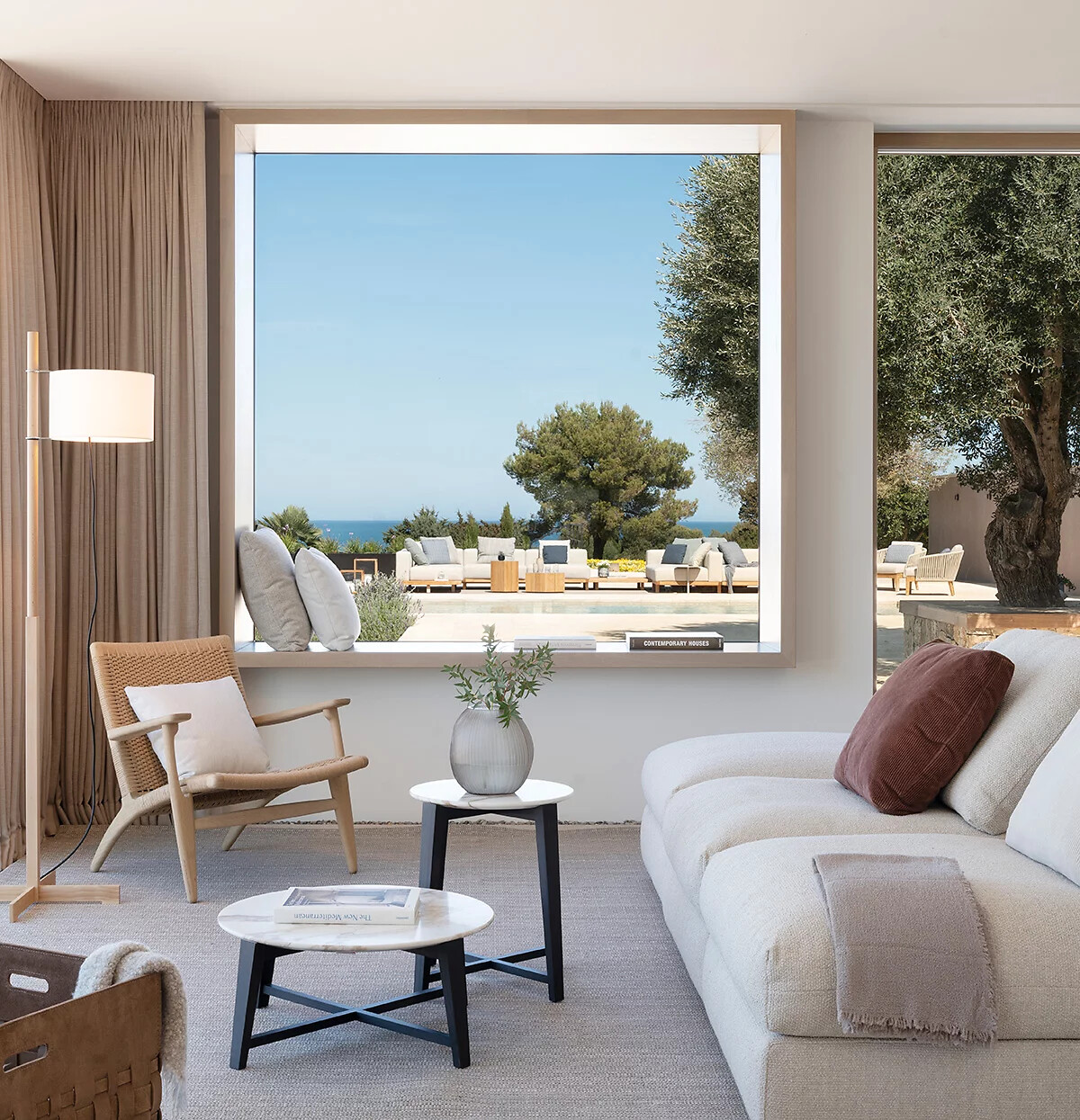 Innenraum mit Sofa und Blick auf Terrasse mit Gartenmöbeln und Meer