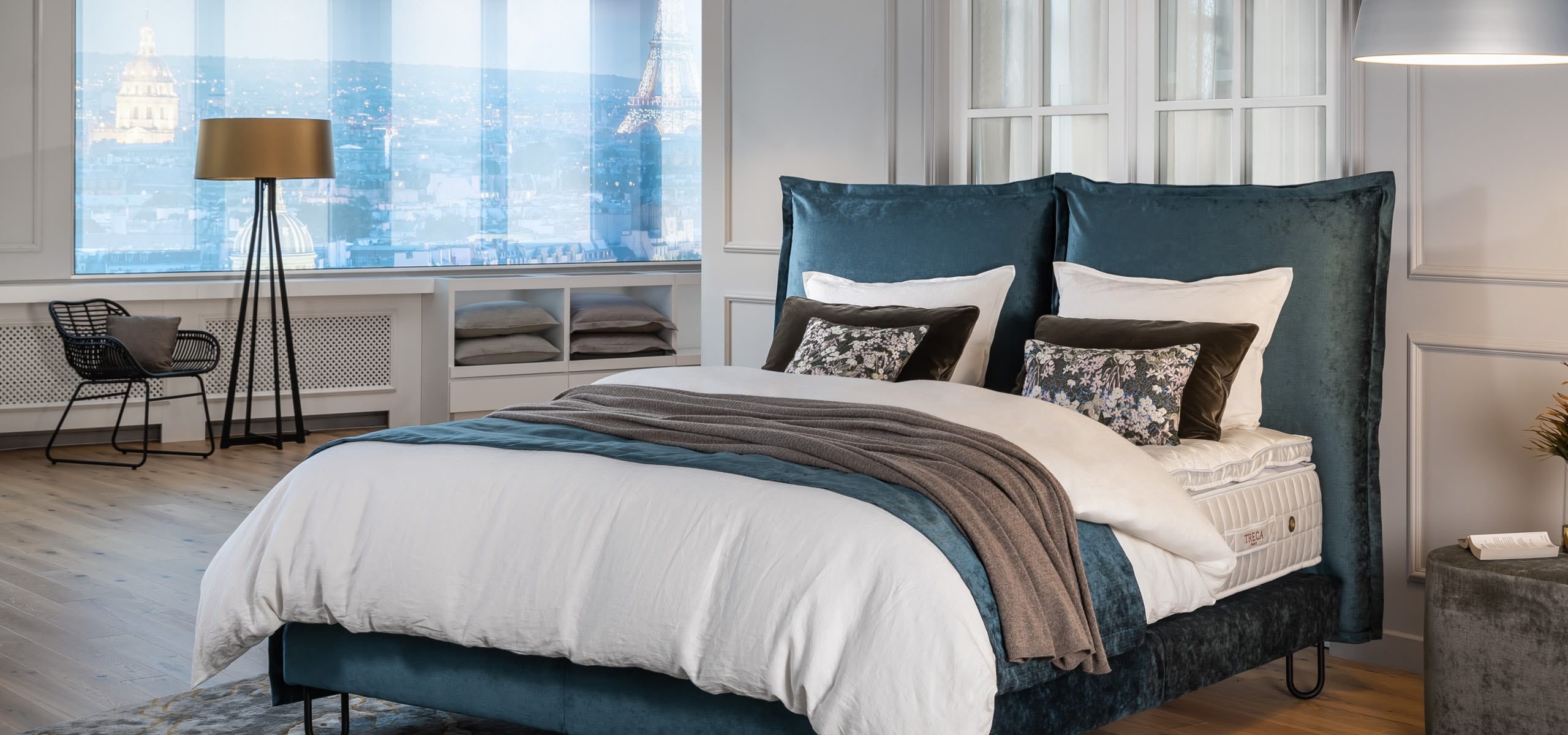 Boxspringbett mit hohem, gepolstertem Kopfteil in Petrol und weißer Bettwäsche auf Holzfußboden