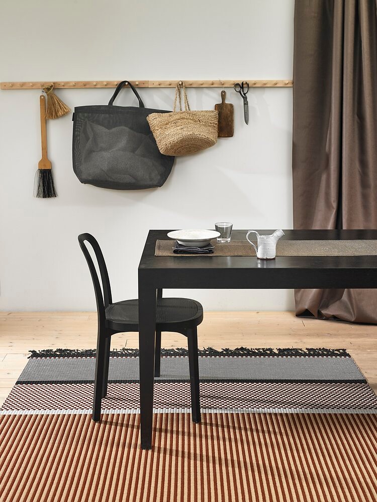 Dunkler Esstisch auf gestreiftem Teppichläufer, Wandhaken mit Taschen im Hintergrund