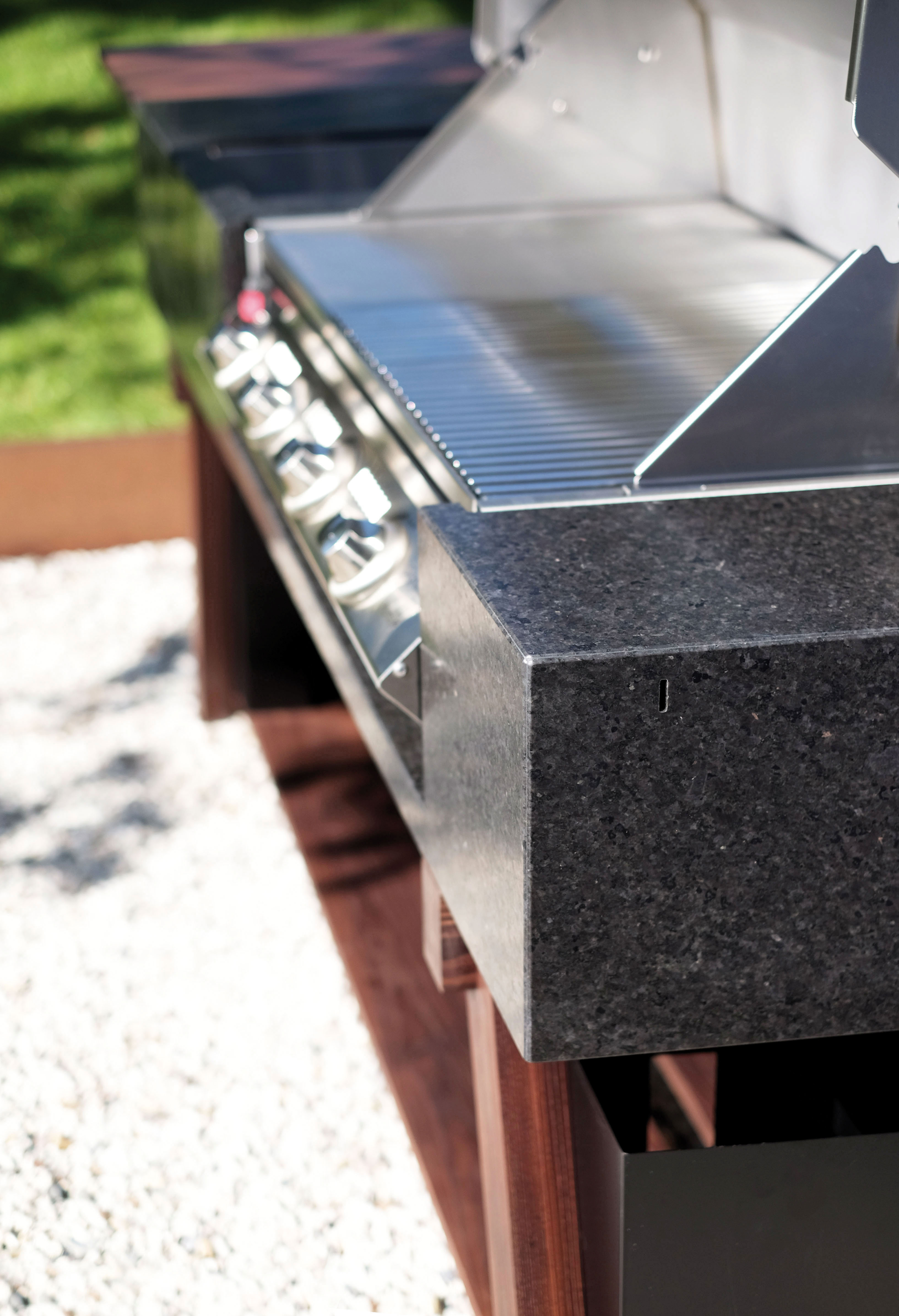 Detailansicht eines eingebauten Edelstahlgrills mit dunkler Steinabdeckung im Garten