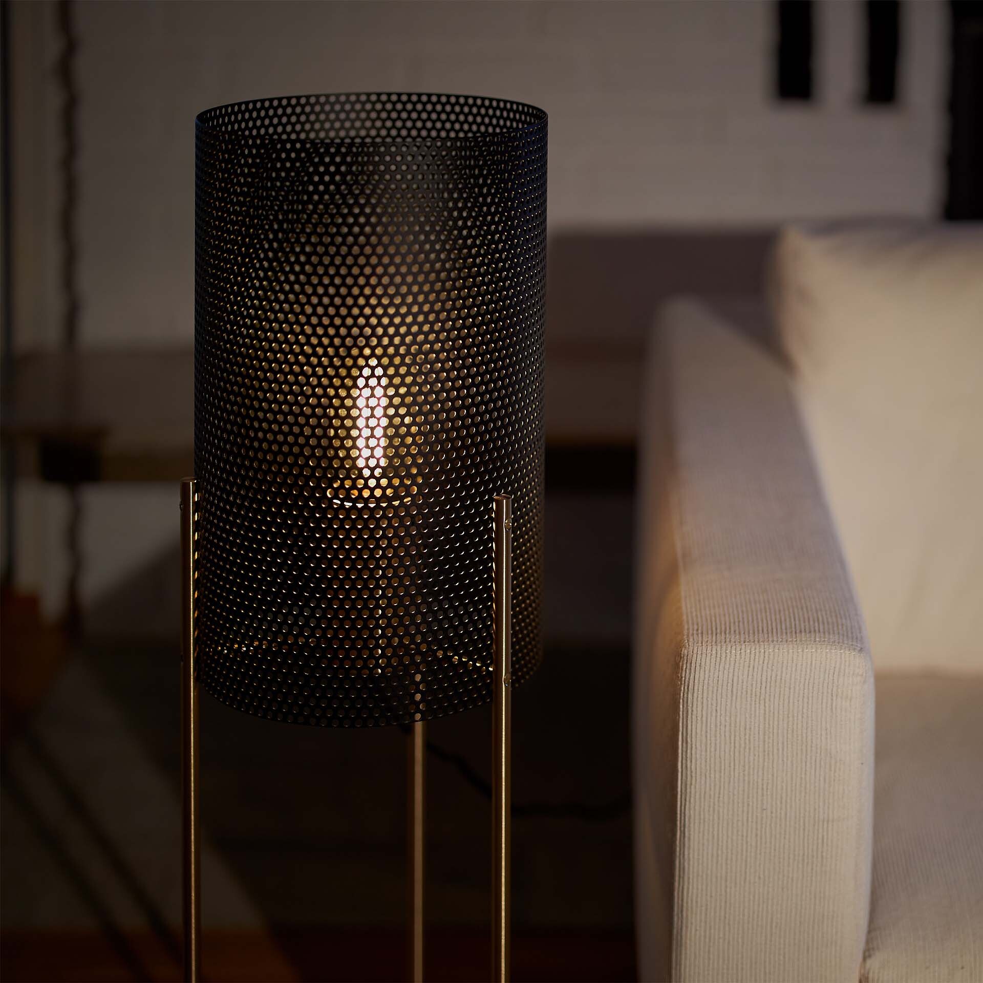 Zylindrische Tischleuchte aus perforiertem Metall mit warmem Licht neben Sofa