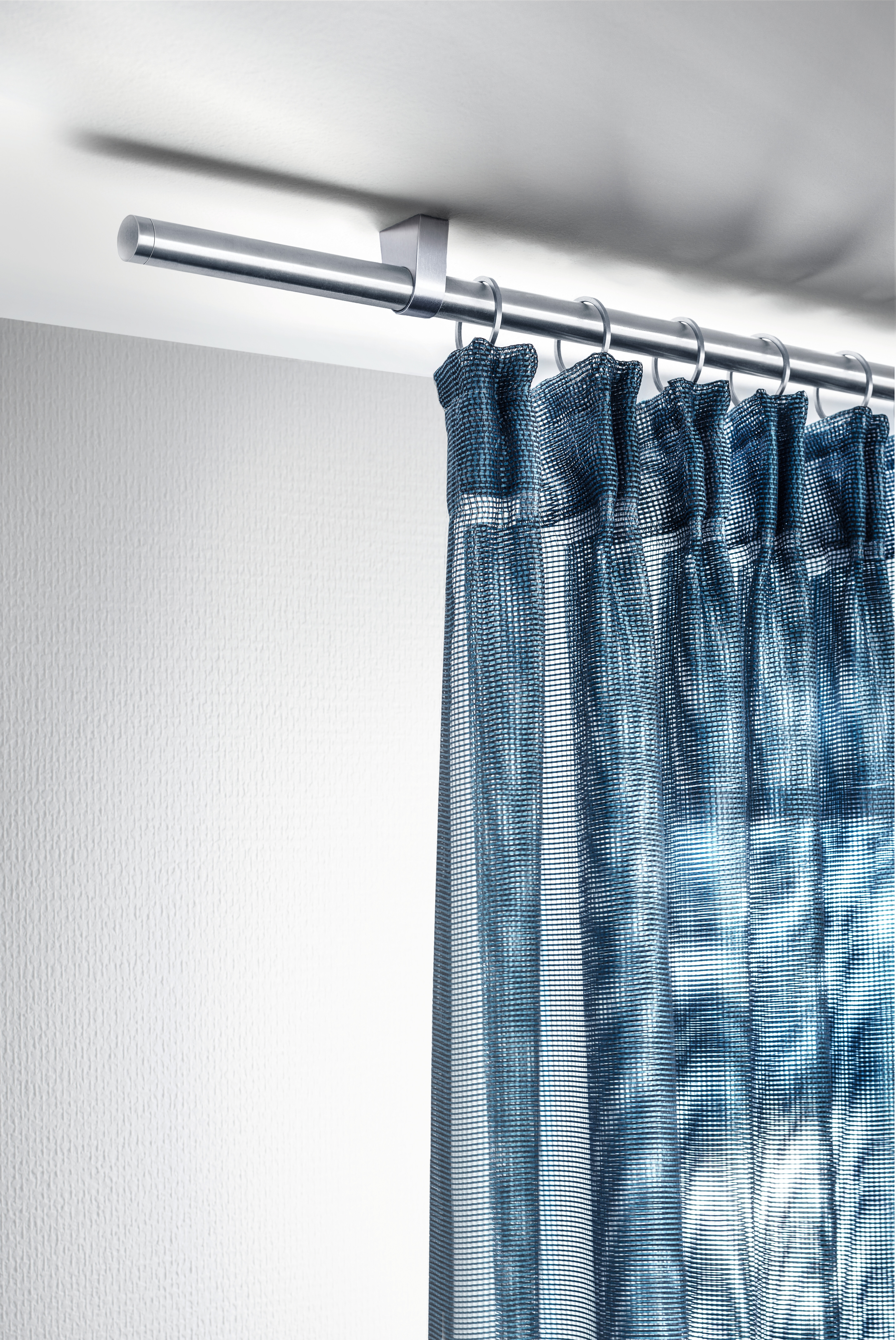 Blau gemusterter Vorhang auf Gardinenstange mit Ringen vor weißer Wand