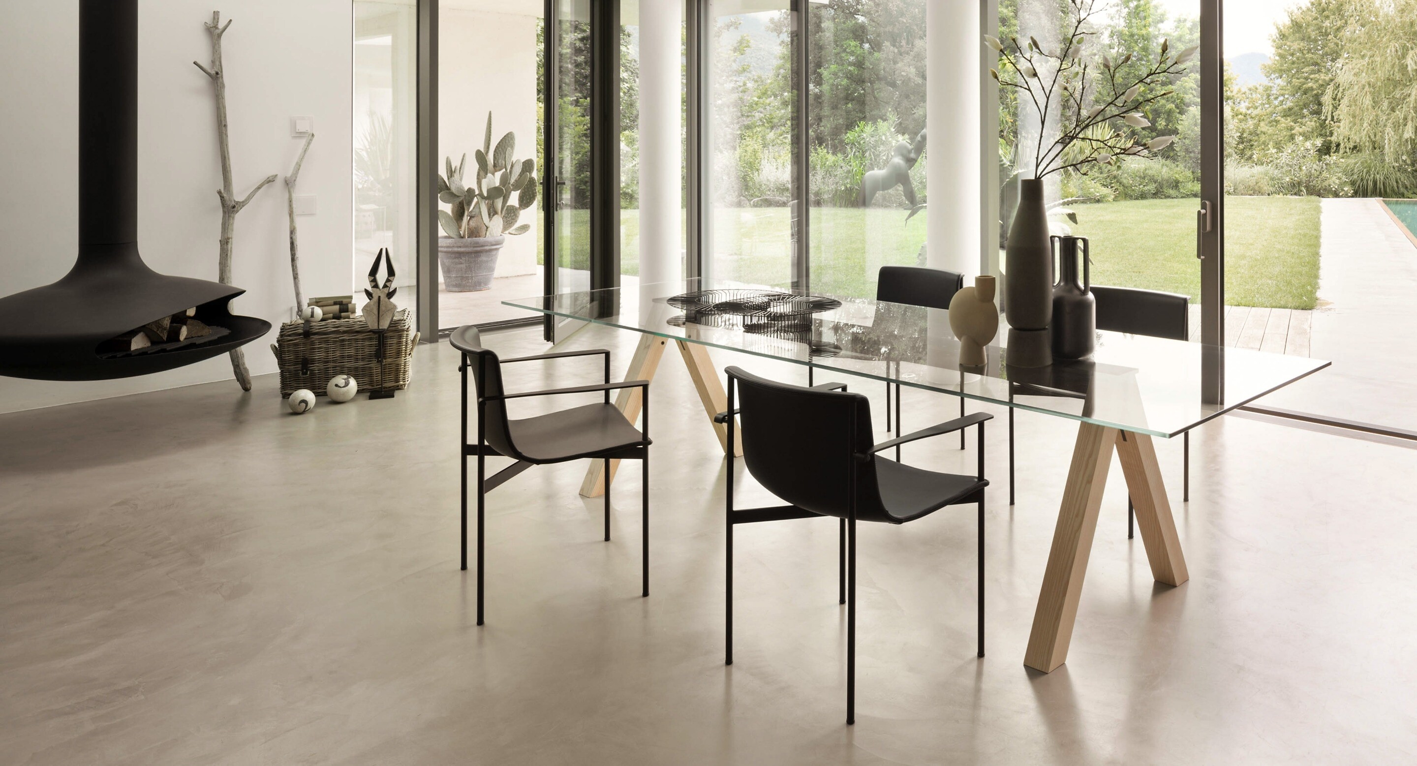 Essbereich mit Glasplatte auf Holzböcken, schwarzen Stühlen und bodentiefer Verglasung