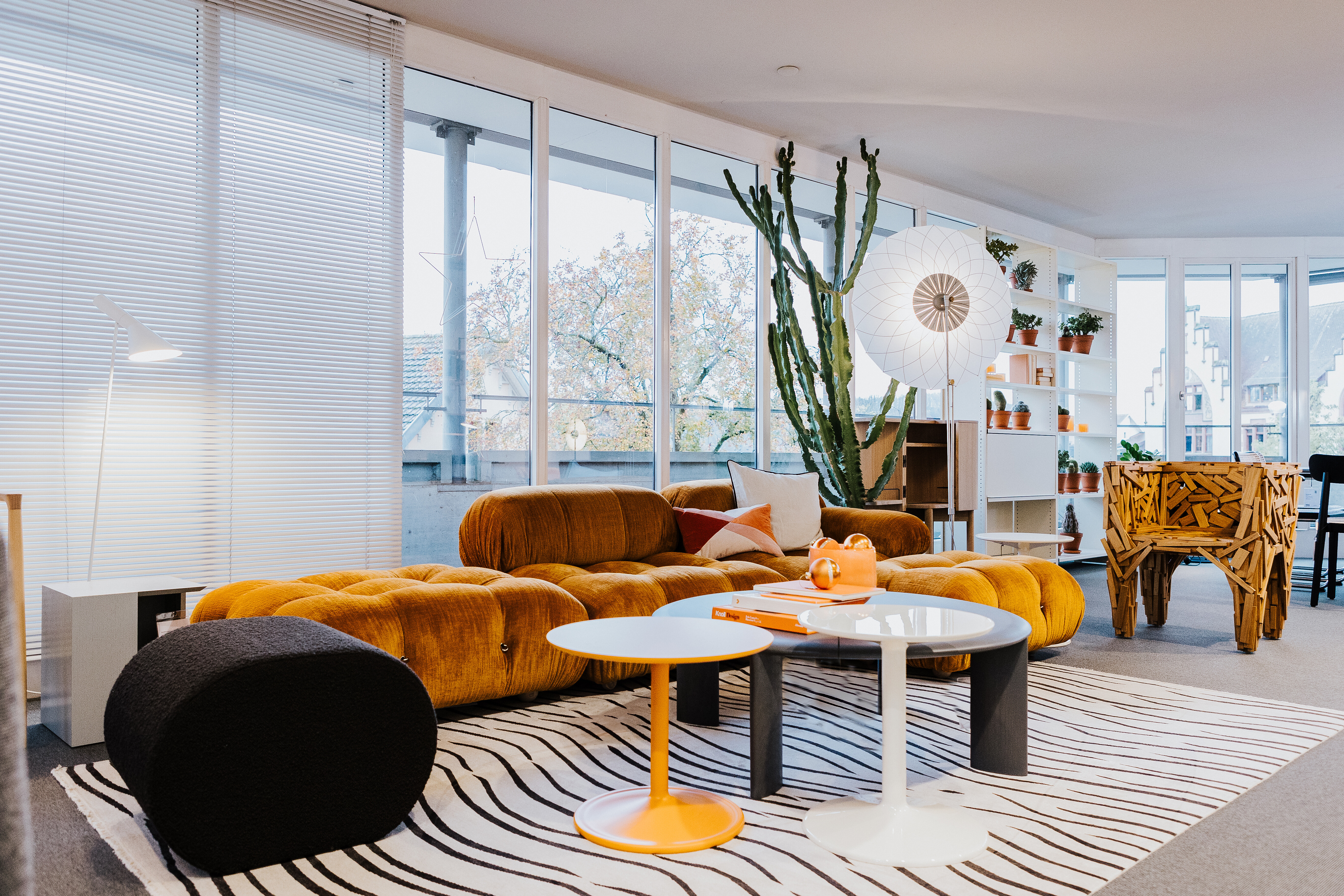 Ausstellungsbereich mit orangefarbenem Sofa, Zebra-Teppich, Beistelltischen und großer Stehleuchte