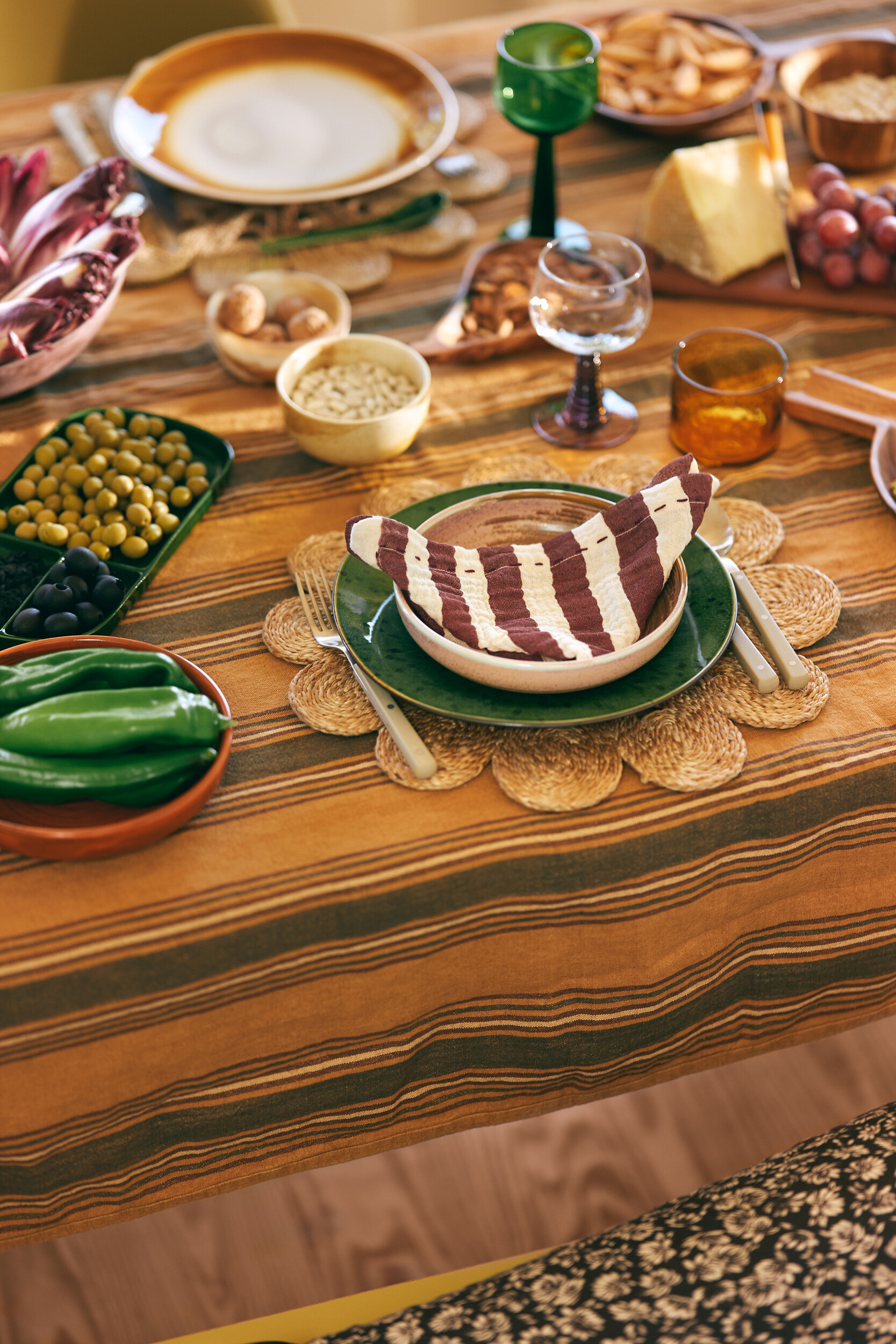 Reich gedeckter Tisch mit gestreifter Decke, Keramik und Gläsern in verschiedenen Farben
