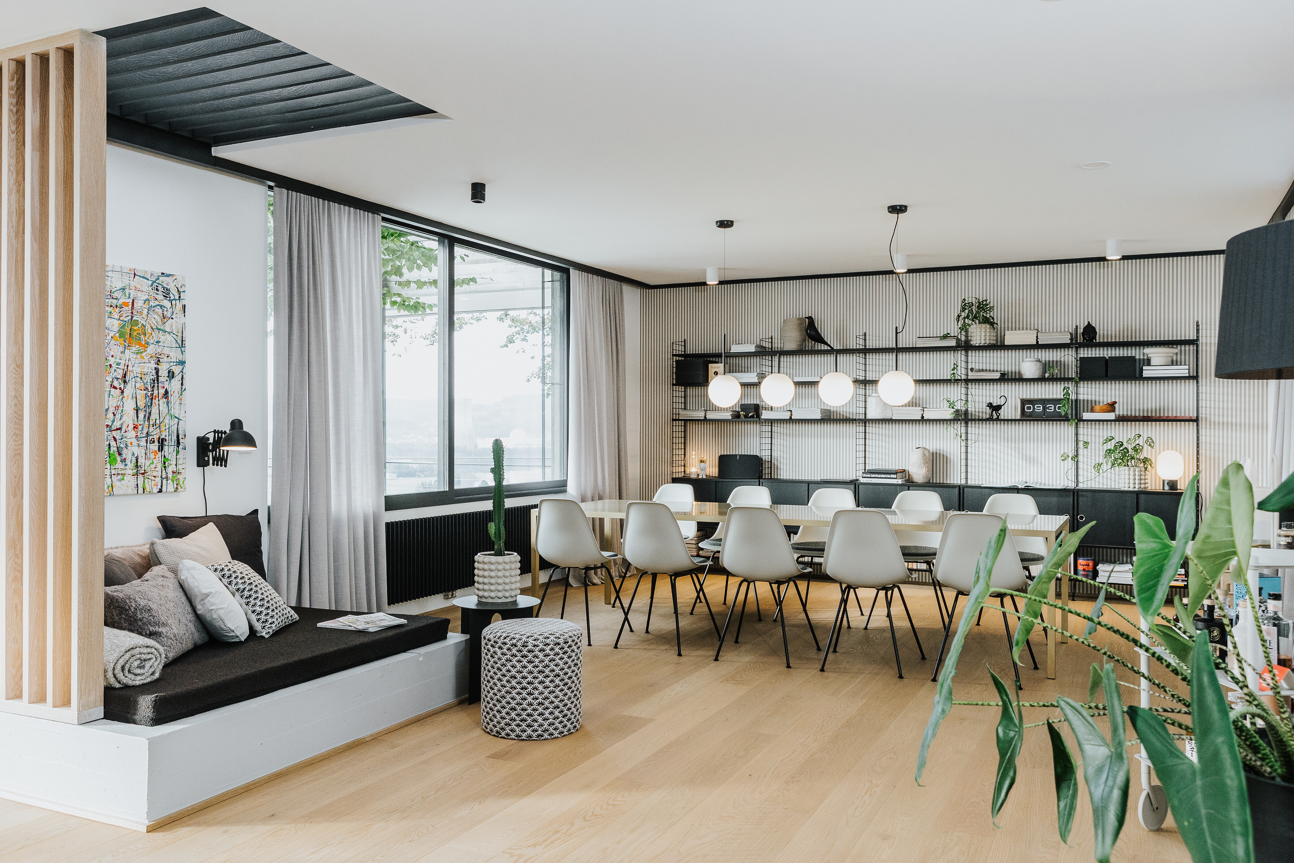 Heller Raum mit langer Tafel, Vitra Stühlen in Weiß und schwarzen Details sowie wohnlicher Sitzecke