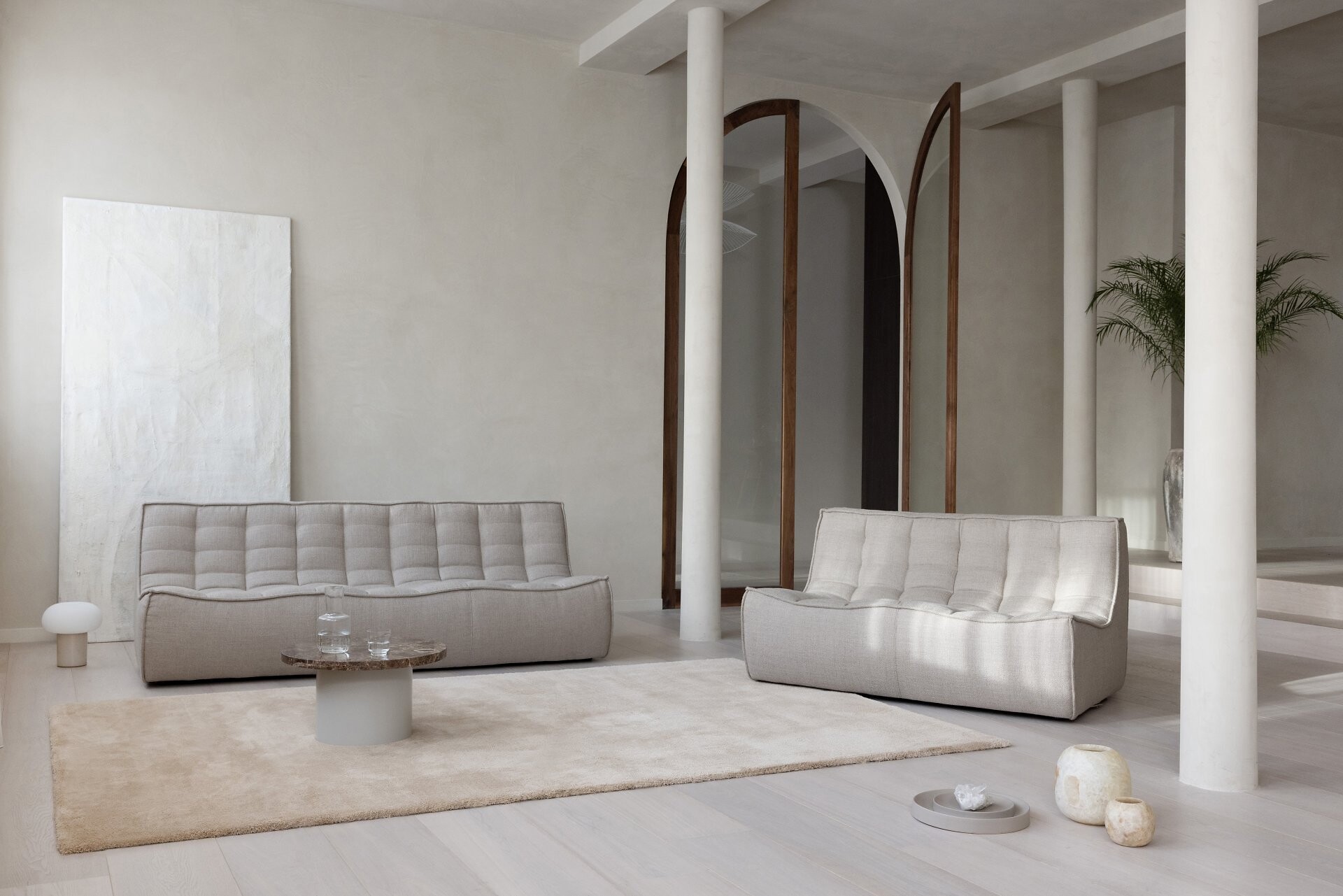 Heller Raum mit Longbarn-Teppich, zwei beigefarbenen Sofas und schlichten geometrischen Wandobjekten