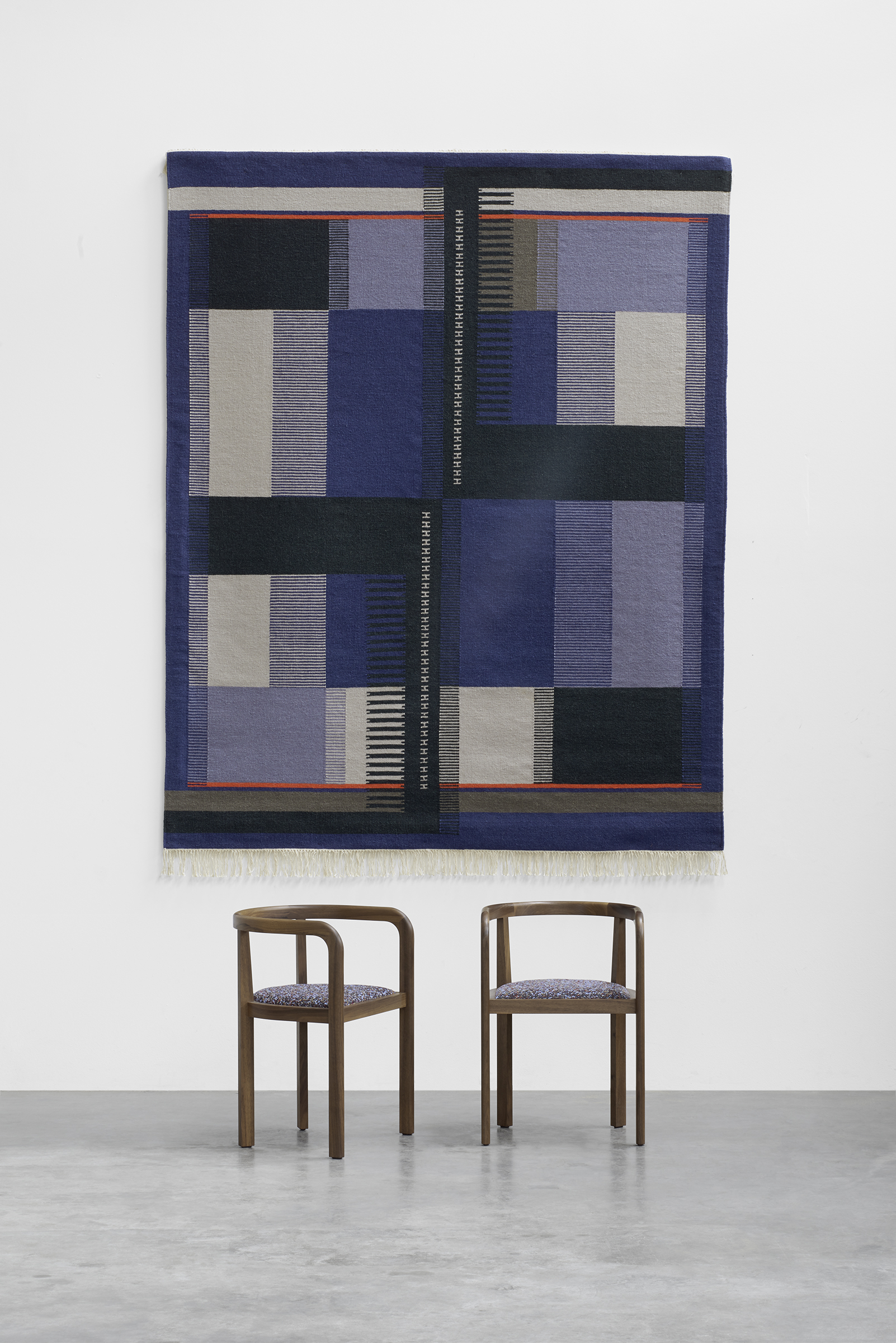 Kvadrat Wandteppich in blau/grau Tönen an Wand vor schwarzen Stühlen