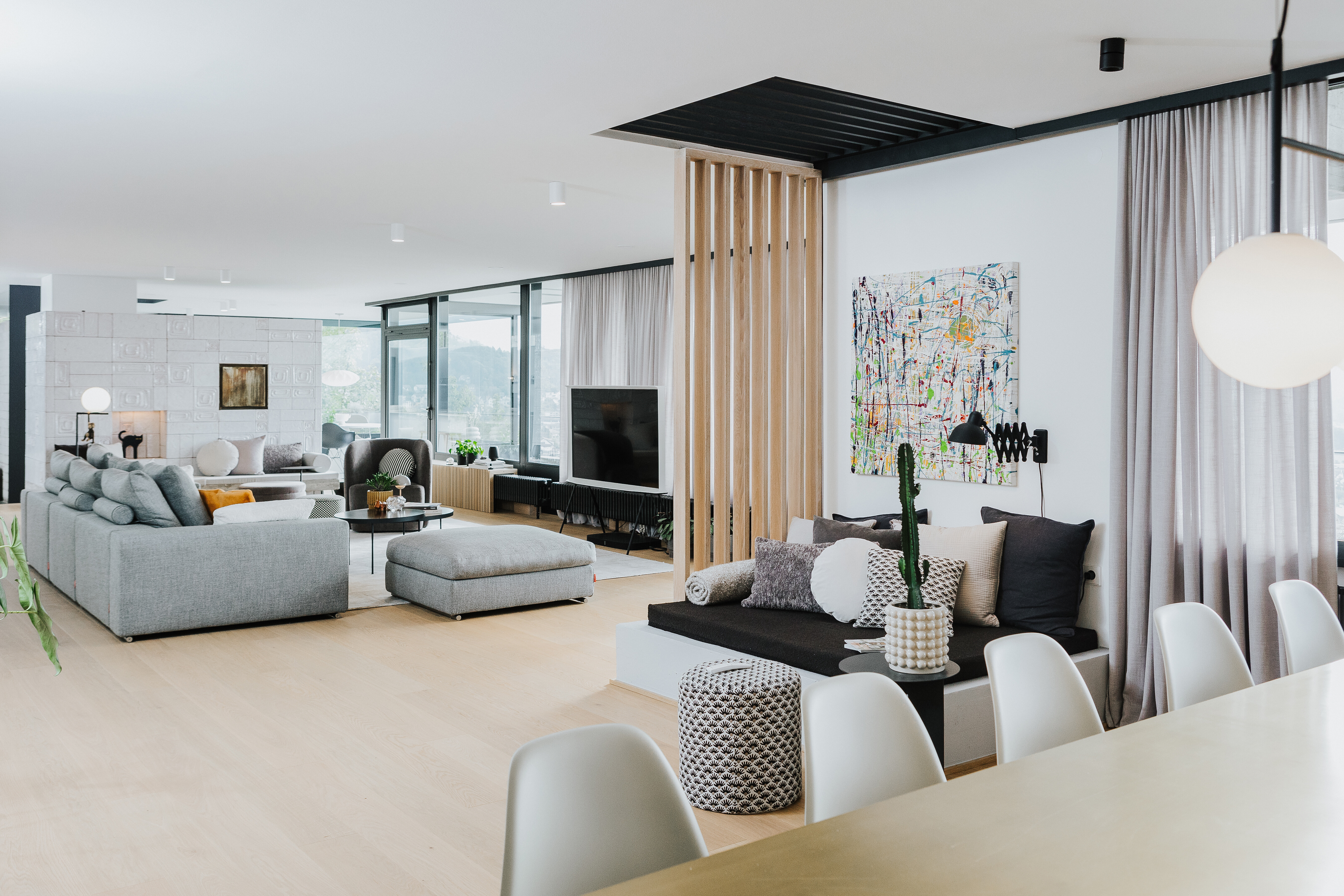 Offener Wohnbereich mit heller Möblierung, abgetrenntem Sitzpodest, grauen Sofas und großem Esstisch.