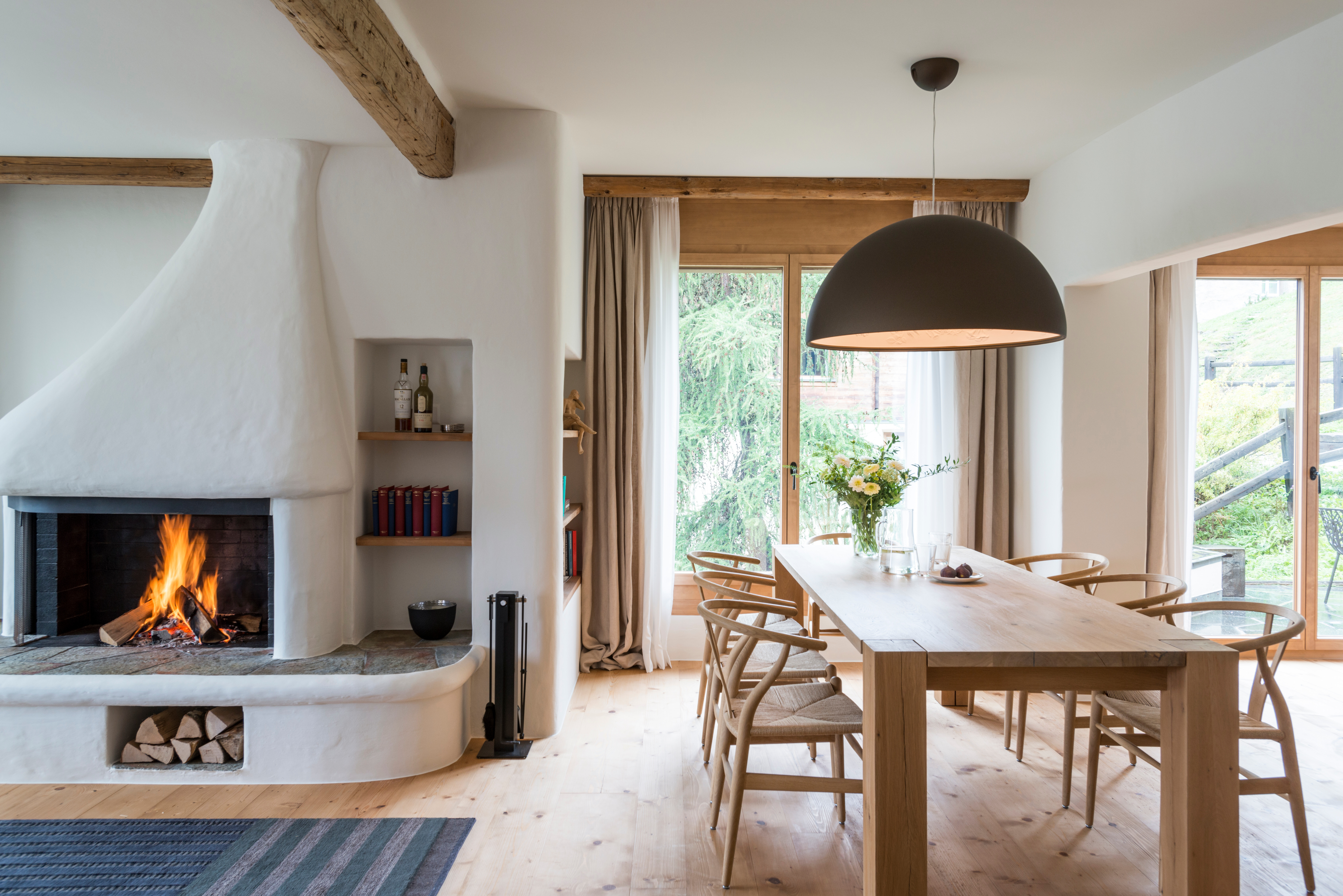 Treffpunkt Esszimmer: Der Holztisch Bigfoot von Philipp Mainzer, sowie die Wishbone Stühle von Carl Hansen unterstreichen den Landhaus Stil. Die Hängeleuchte Skygarden von Flos bildet einen schönen Gegensatz.