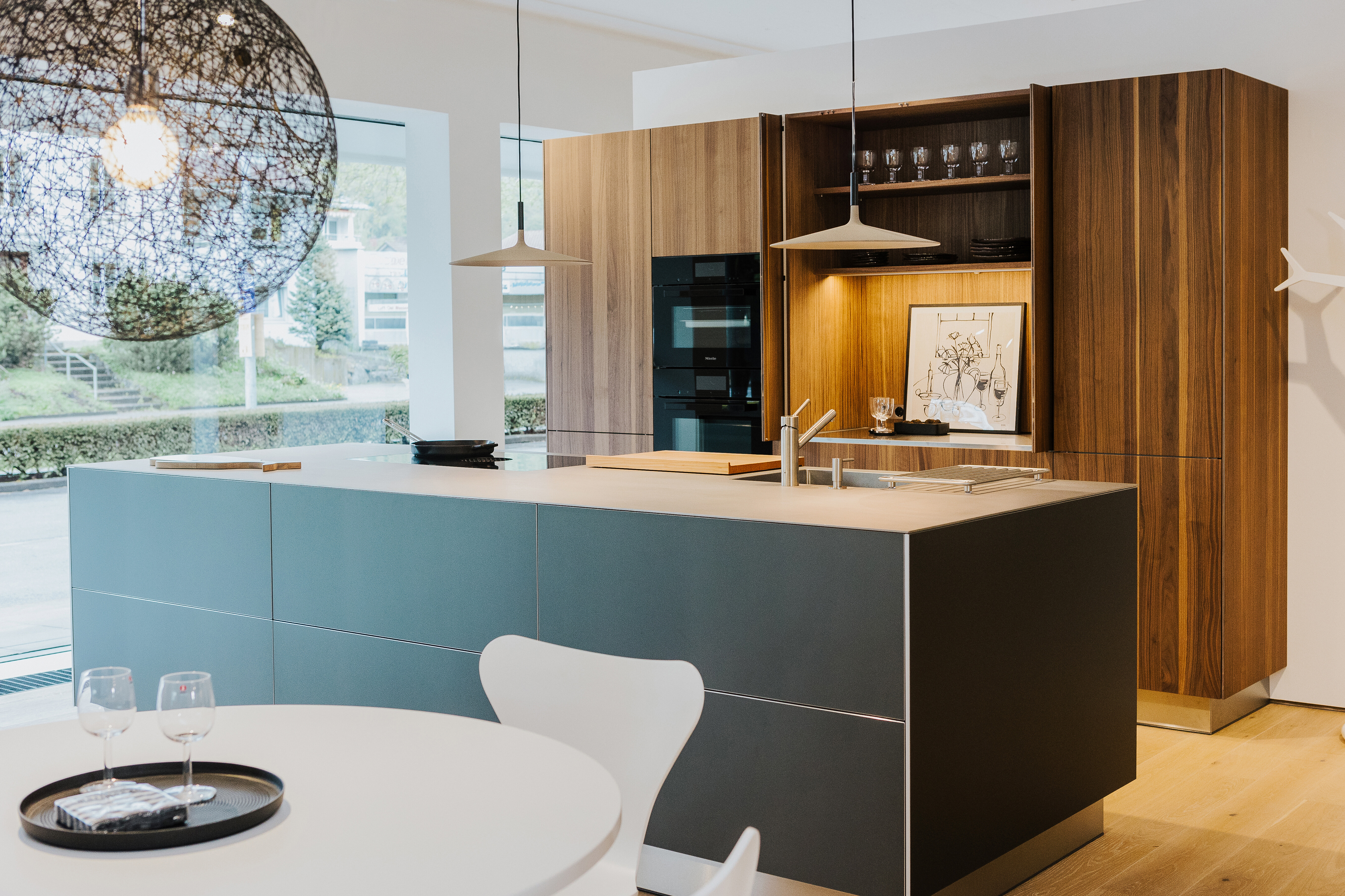 Offene Wohnküche mit Kücheninsel in Dunkelgrau und Hochschränken in Nussbaumoptik mit Regalnische