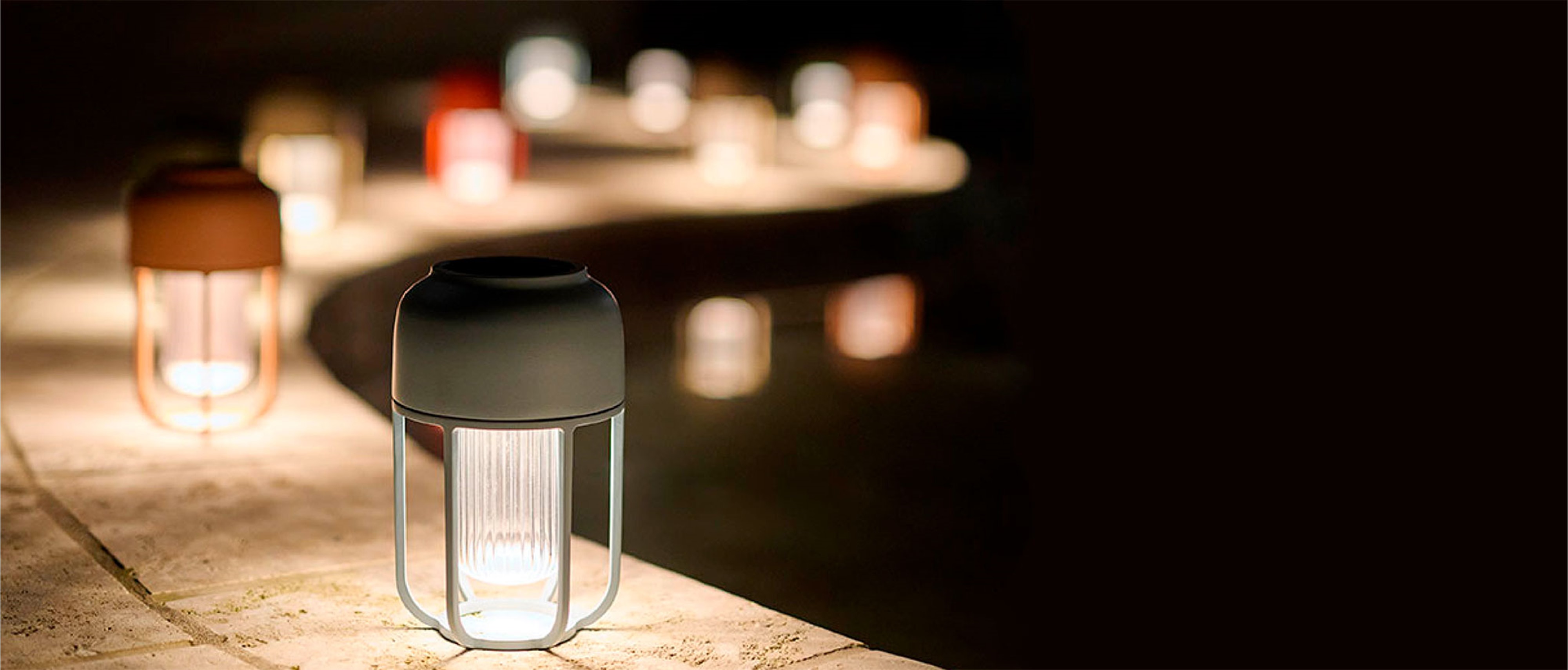 Mehrere Solarleuchten Light No1 von Houe leuchten abends entlang einer geschwungenen Mauer.