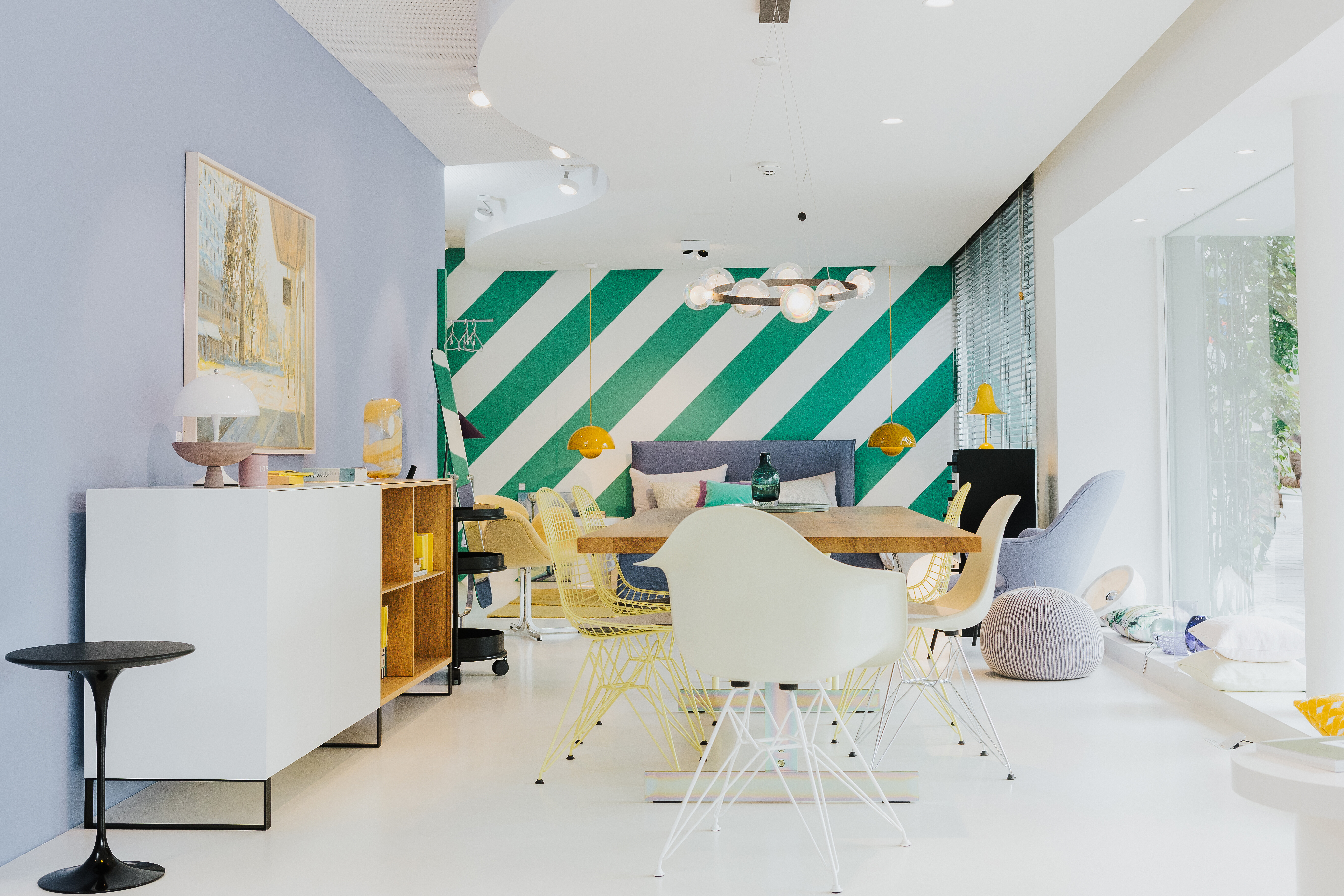 Blick in farbenfrohen Ausstellungsbereich mit Streifenwand, Essplatz und Lounge-Möbeln